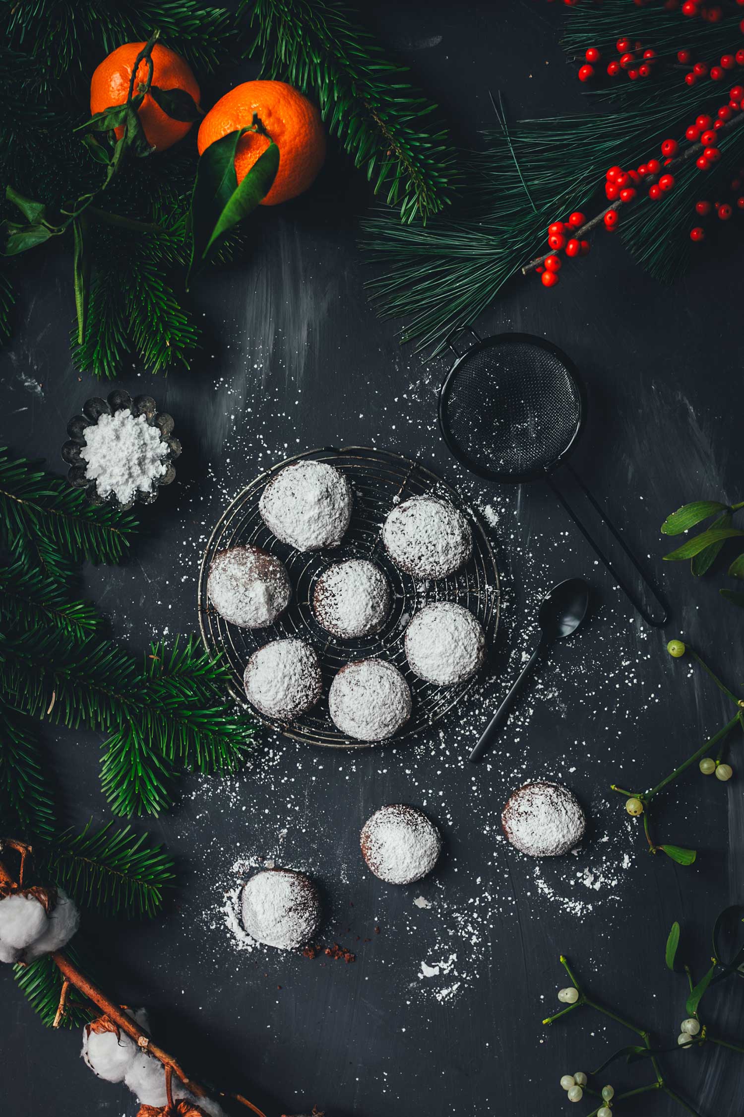 Espresso-Walnuss-Kekse von oben fotografiert, auf einem Gitter mit Puderzucker und stimmungsvoller Weihnachtsdeko aus Tannengrün und Beeren.