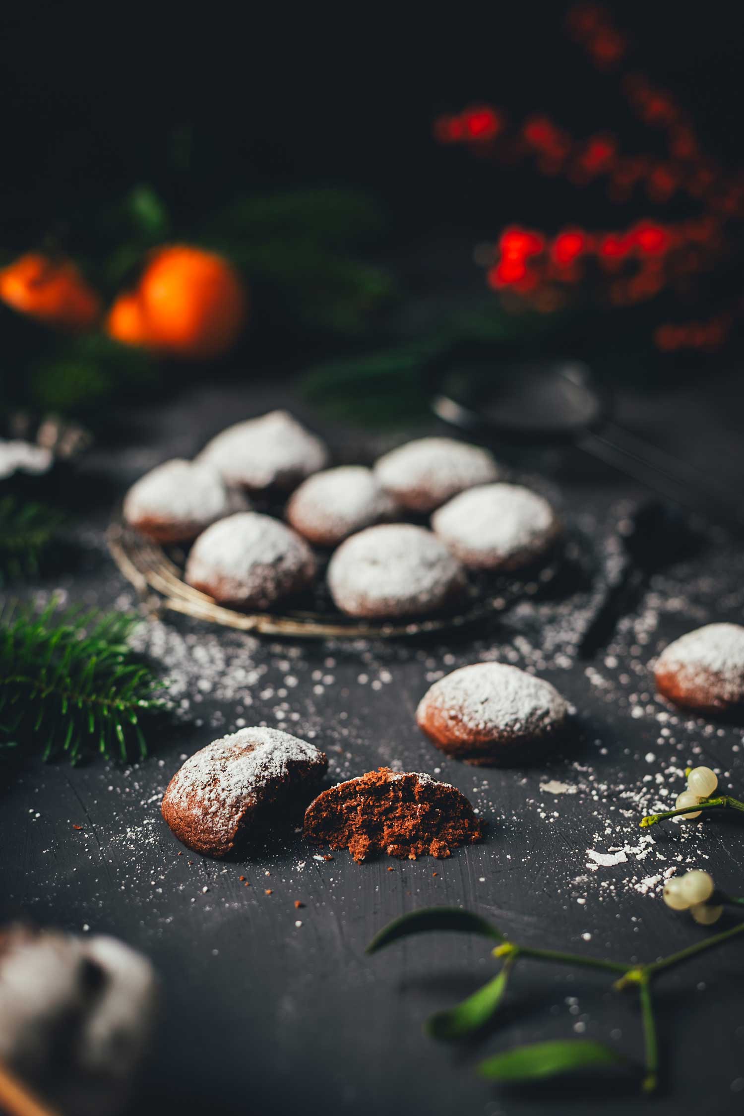 Espresso-Walnuss-Kekse im Vordergrund, angeschnitten und mit Puderzucker bestäubt, dahinter unscharf ein Teller mit weiteren Keksen und weihnachtlichen Elementen.