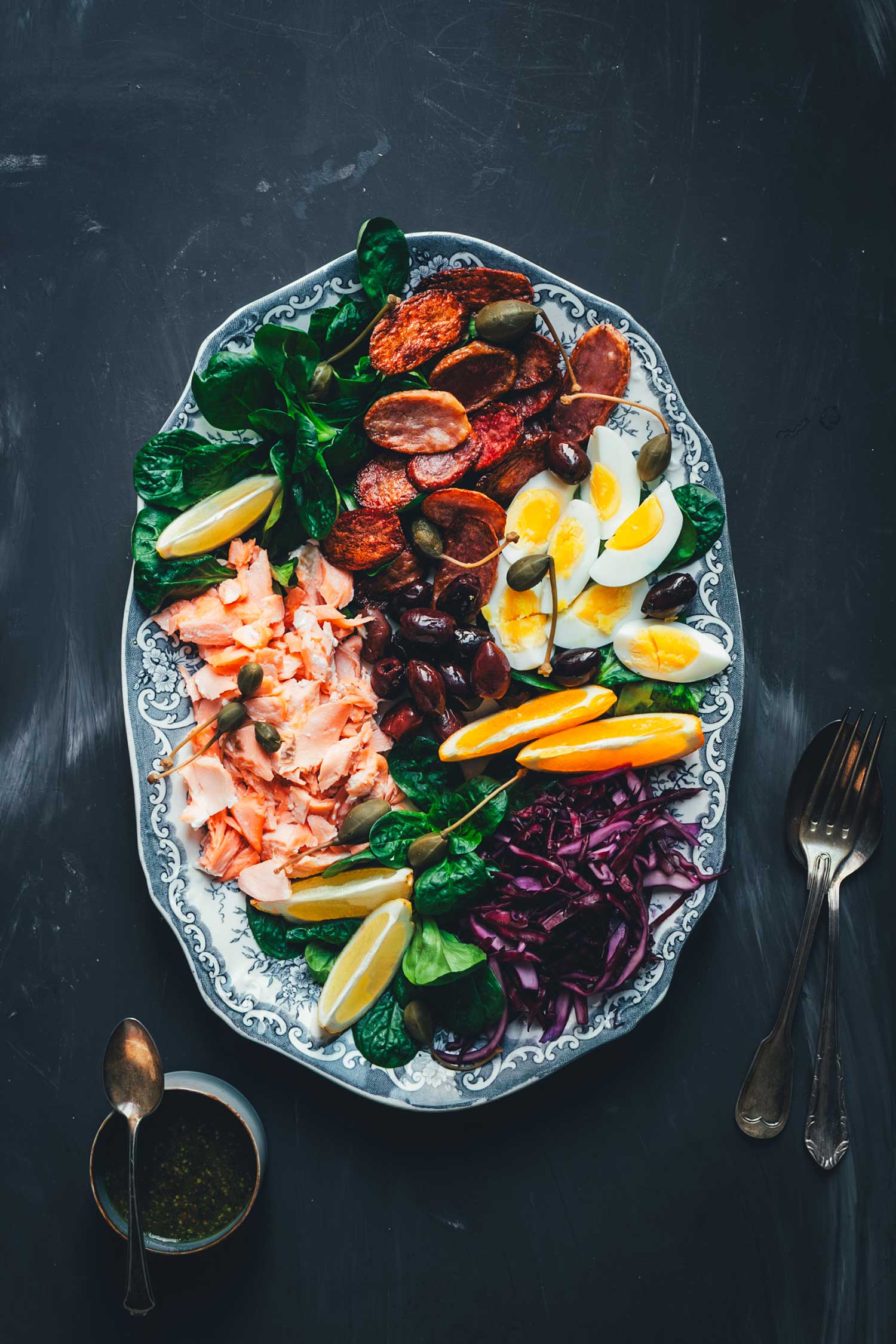Clkeaner Topshot Winterlicher Nizza Salat mit Pulled Lachs auf Servierplatte – mit Rotkohl, Feldsalat, knusprigen Kartoffeln, Eiern, Orangen und Kapernäpfeln.