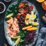 Winterlicher Nizza Salat mit Pulled Lachs auf Servierplatte – mit Rotkohl, Feldsalat, knusprigen Kartoffeln, Eiern, Orangen und Kapernäpfeln.