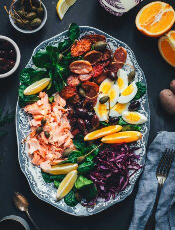 Winterlicher Nizza Salat mit Pulled Lachs auf Servierplatte – mit Rotkohl, Feldsalat, knusprigen Kartoffeln, Eiern, Orangen und Kapernäpfeln.
