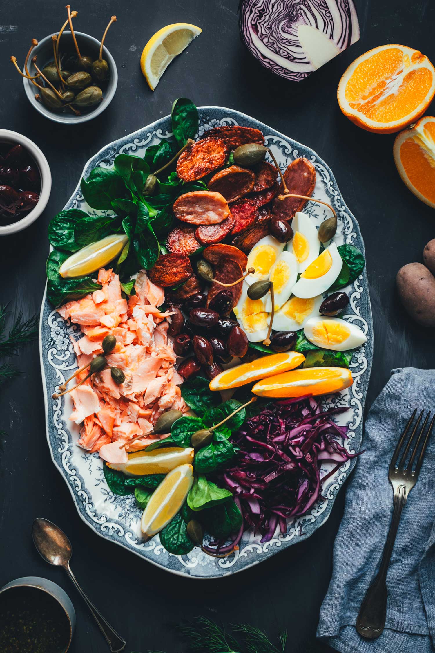Winterlicher Nizza Salat mit Pulled Lachs auf Servierplatte – mit Rotkohl, Feldsalat, knusprigen Kartoffeln, Eiern, Orangen und Kapernäpfeln.
