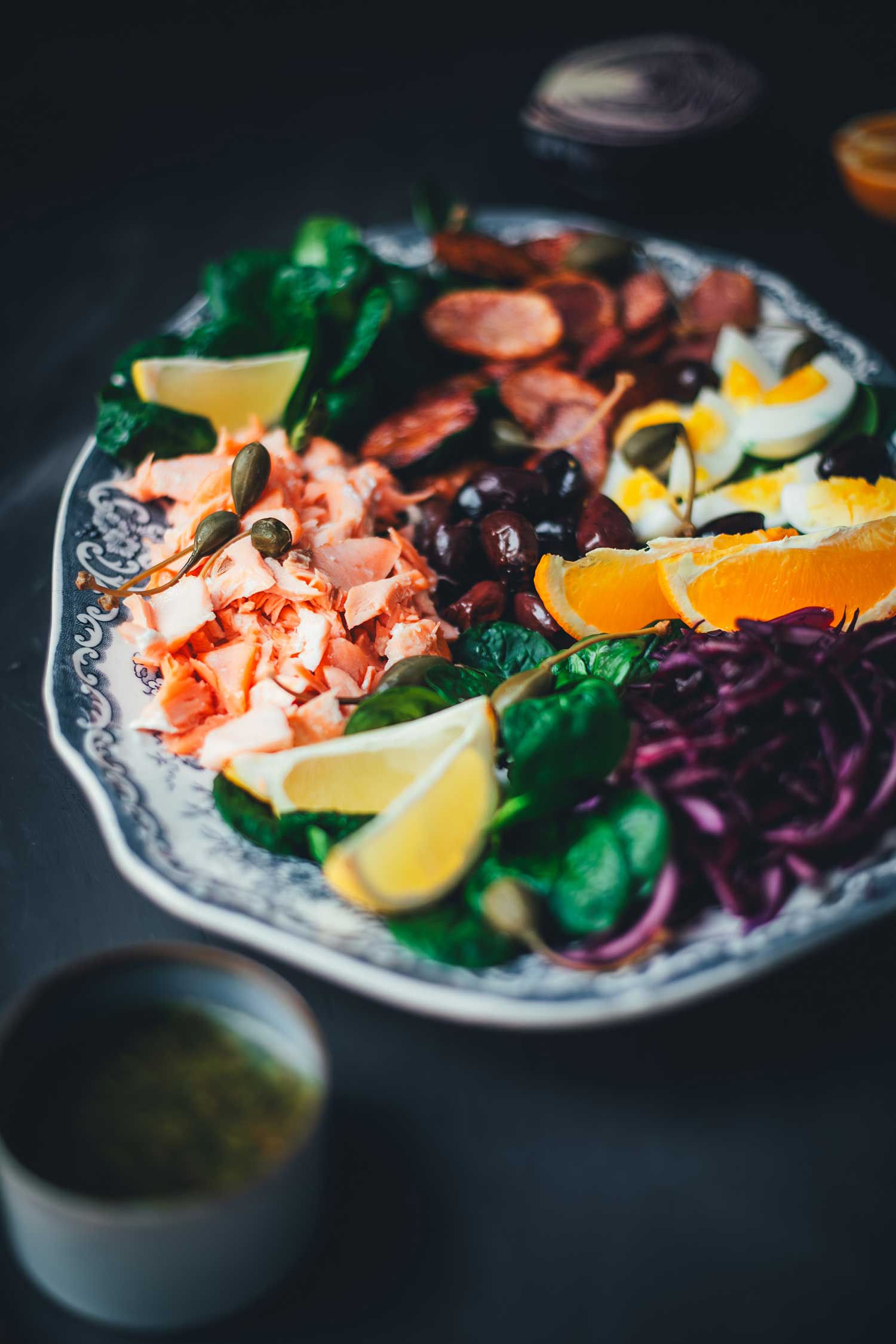 Seitliche Ansicht Winterlicher Nizza Salat mit Pulled Lachs auf Servierplatte – mit Rotkohl, Feldsalat, knusprigen Kartoffeln, Eiern, Orangen und Kapernäpfeln.