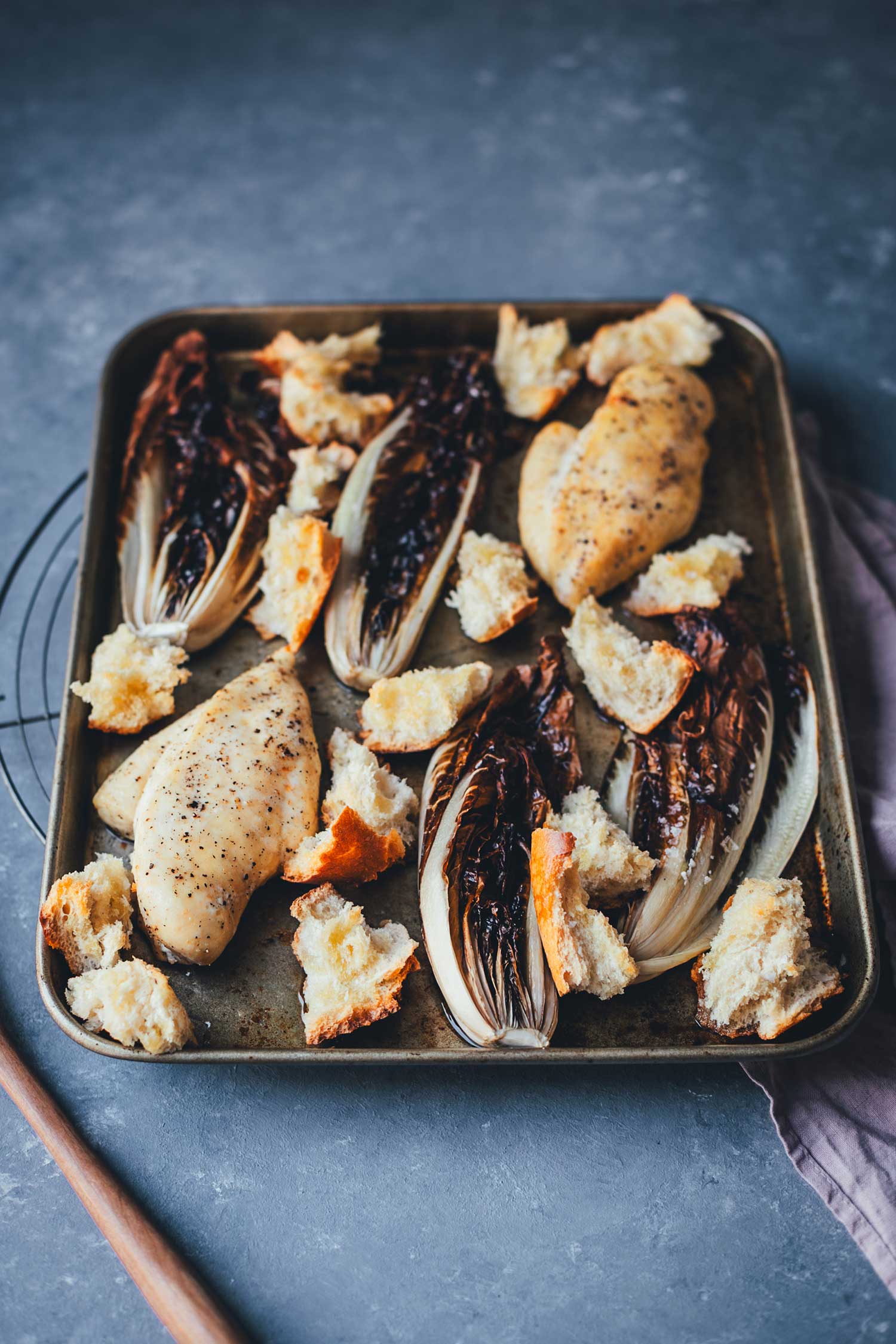 Seitliche Draufsicht auf das fertige Blechgericht mit Hähnchenbrust, Radicchio vom Blech und Croutons, unmittelbar vor dem Servieren