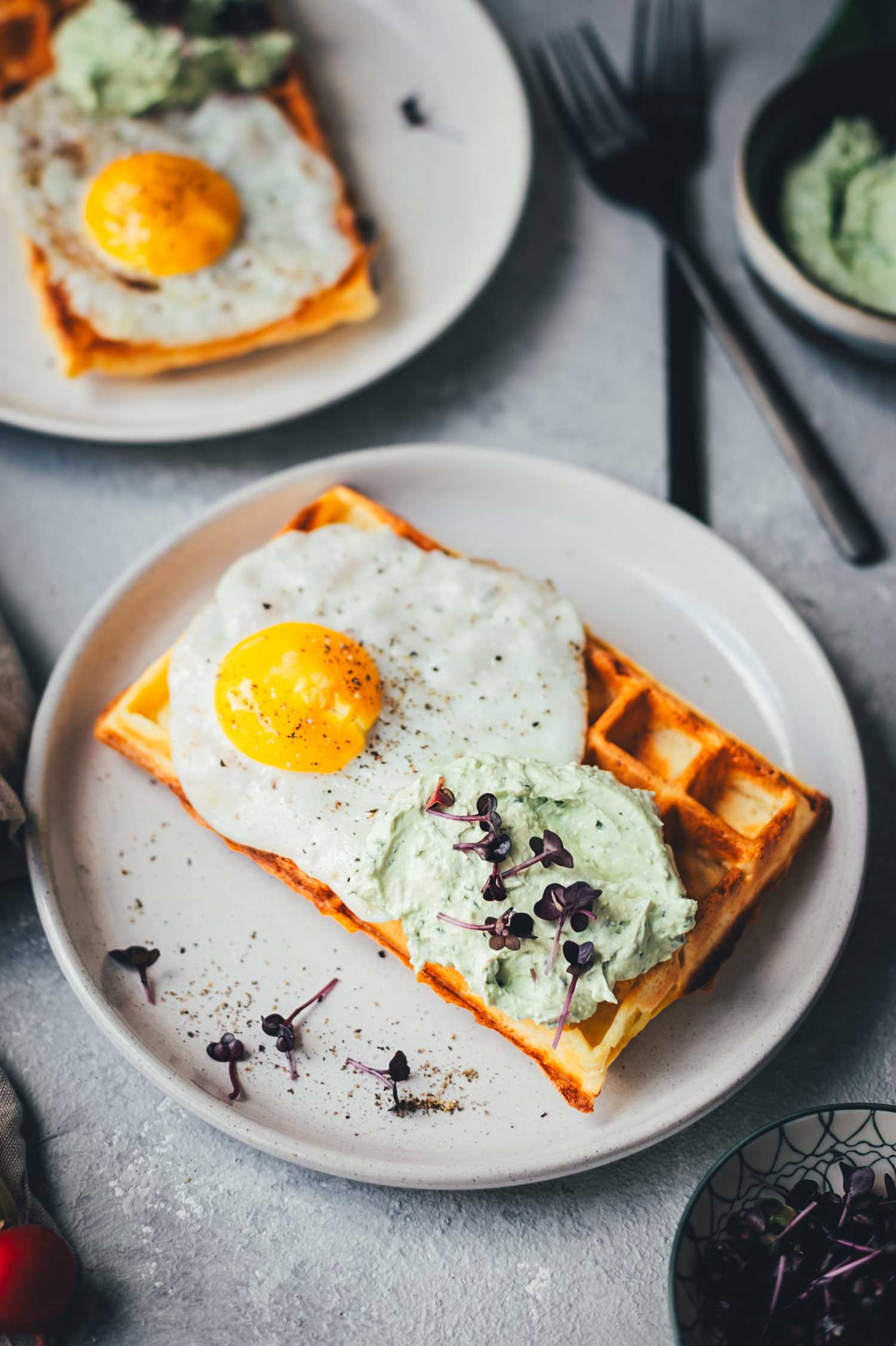 Nahaufnahme von einem hellen Teller mit einer frisch gebackenen Kartoffel-Waffel, die herzhaft mit Spiegelei und Bärlauch-Feta-Dip serviert wird. 
