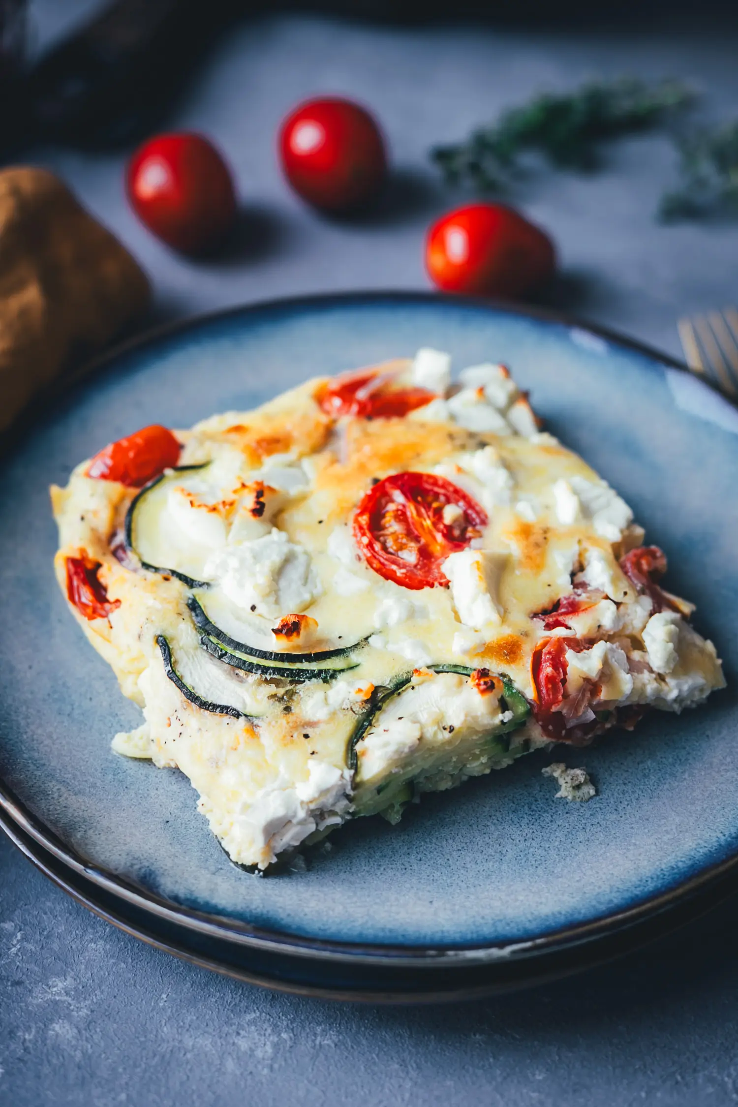 : Anschnitt eines Stücks Zucchini-Frittata mit Feta, bei dem die dünnen Zucchinischeiben und die saftige Eiermasse zu sehen sind.