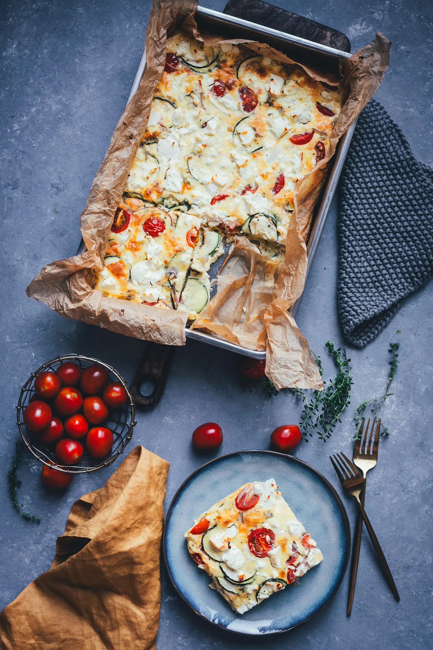 Zucchini-Frittata mit Feta und Tomaten in der Form, ein Stück herausgeschnitten und auf einem Teller angerichtet.