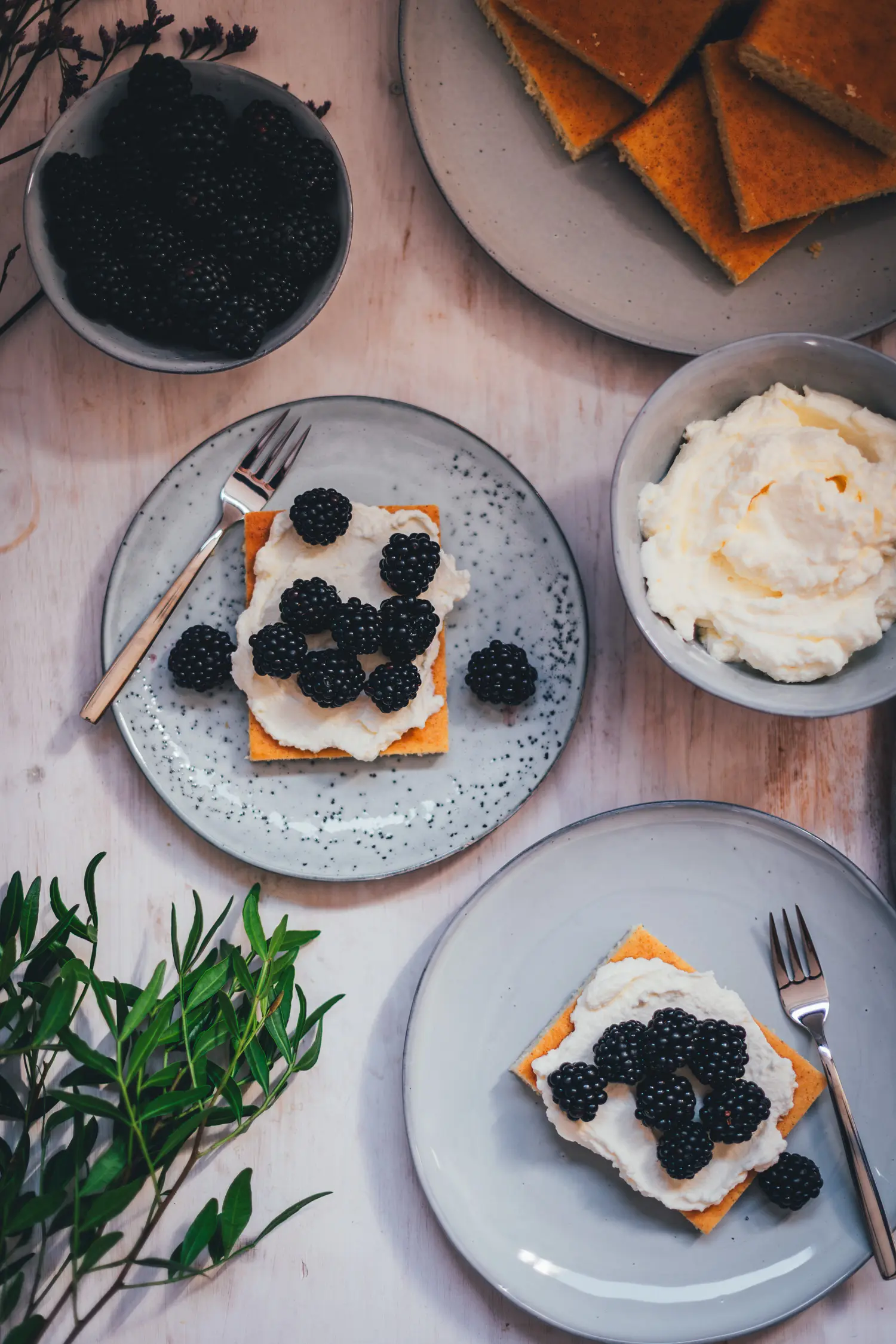 Hot Milk Sponge Cake in Stücken mit Mascarpone-Creme und Brombeeren, dazu eine Schale frischer Brombeeren und geschlagene Mascarpone-Creme von oben fotografiert.