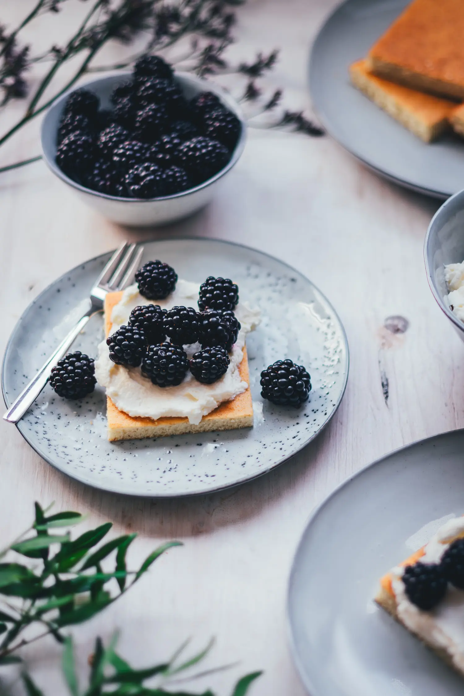 Hot Milk Sponge Cake mit Mascarpone-Creme und Brombeeren auf einem Teller, daneben eine Schale Brombeeren und geschlagene Creme.
