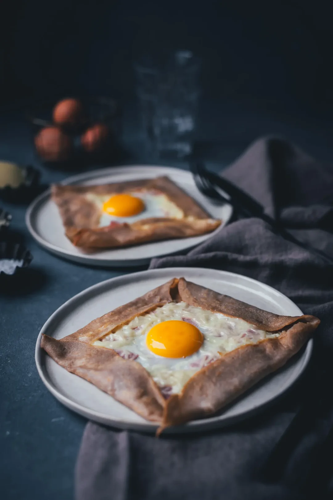 Seitliche Ansicht von zwei Tellern mit frisch gebackenen Galettes Complètes – französischen Buchweizenpfannkuchen aus der Bretagne, die mit Käse, Schinken und Spiegelei gefüllt sind.