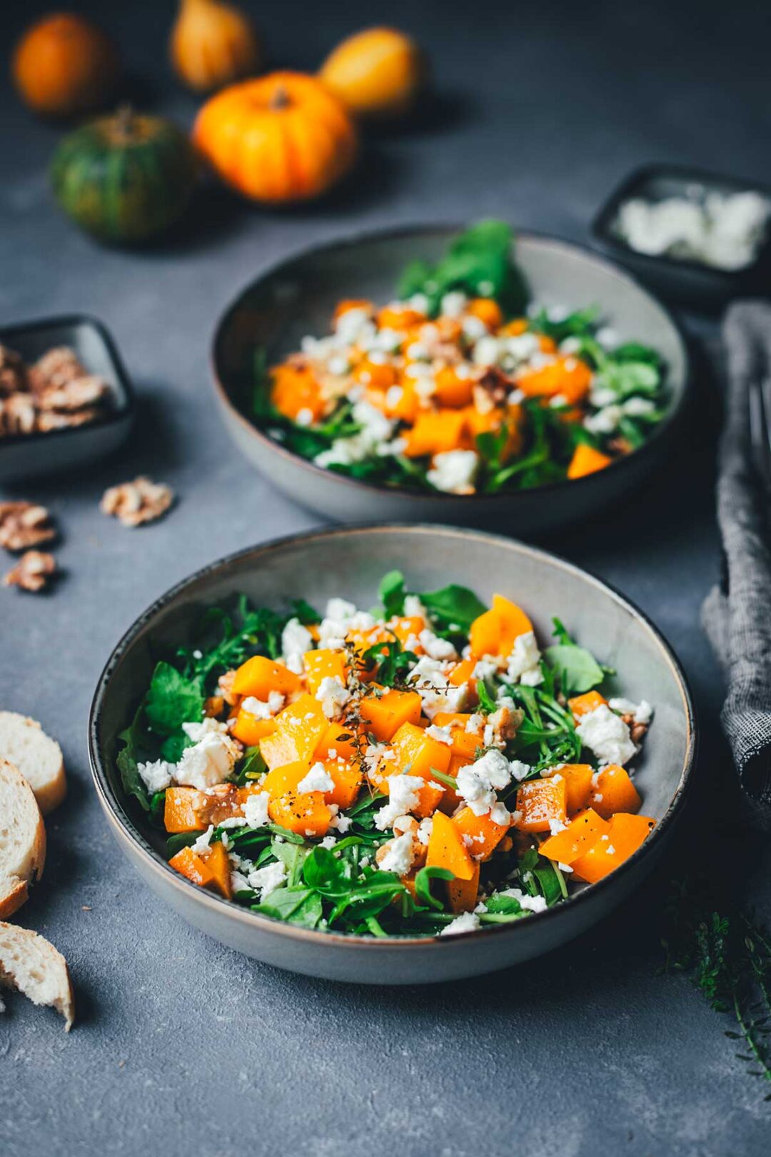 Kürbis-Salat auf zwei tiefen Tellern angerichtet – goldbraun gerösteter Butternut-Kürbis auf Rucola, garniert mit Walnusskernen und Feta, serviert mit knusprigem Brot | moeyskitchen.com