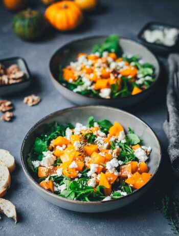 Kürbis-Salat auf zwei tiefen Tellern angerichtet – goldbraun gerösteter Butternut-Kürbis auf Rucola, garniert mit Walnusskernen und Feta, serviert mit knusprigem Brot | moeyskitchen.com