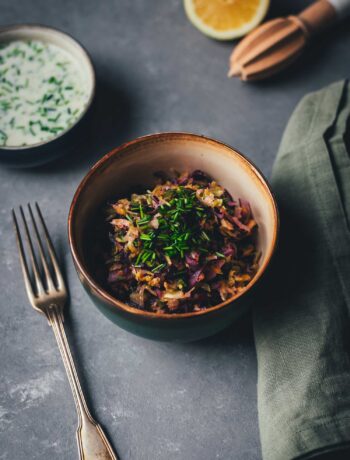 Krautsalat in Keramikschale mit Schnittlauch, daneben Gabel und Leinentuch – im Hintergrund Zitrone und Buttermilch-Zitronen-Dressing.