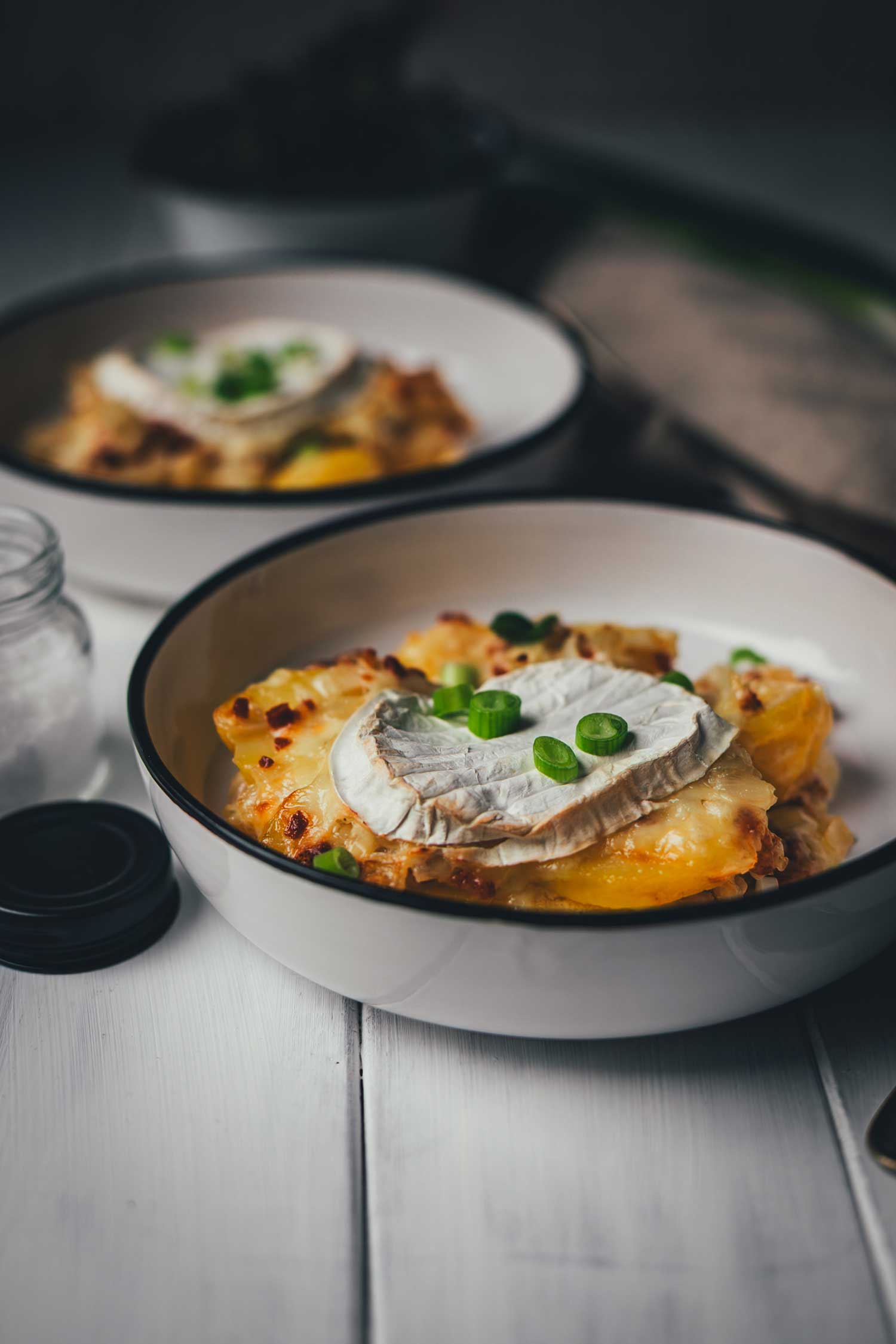 Detailaufnahme einer Portion Tartiflette: Der weiche, geschmolzene Kern des Camemberts fließt über die goldgelben Kartoffelscheiben und krossen Speckwürfel.