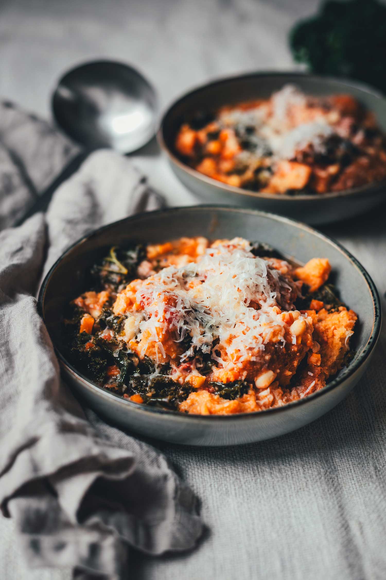 Nahaufnahme eines Tellers mit Eintopf, dick bestreut mit frisch geriebenem Parmesan, darunter ein graues Küchentuch | moeyskitchen.com