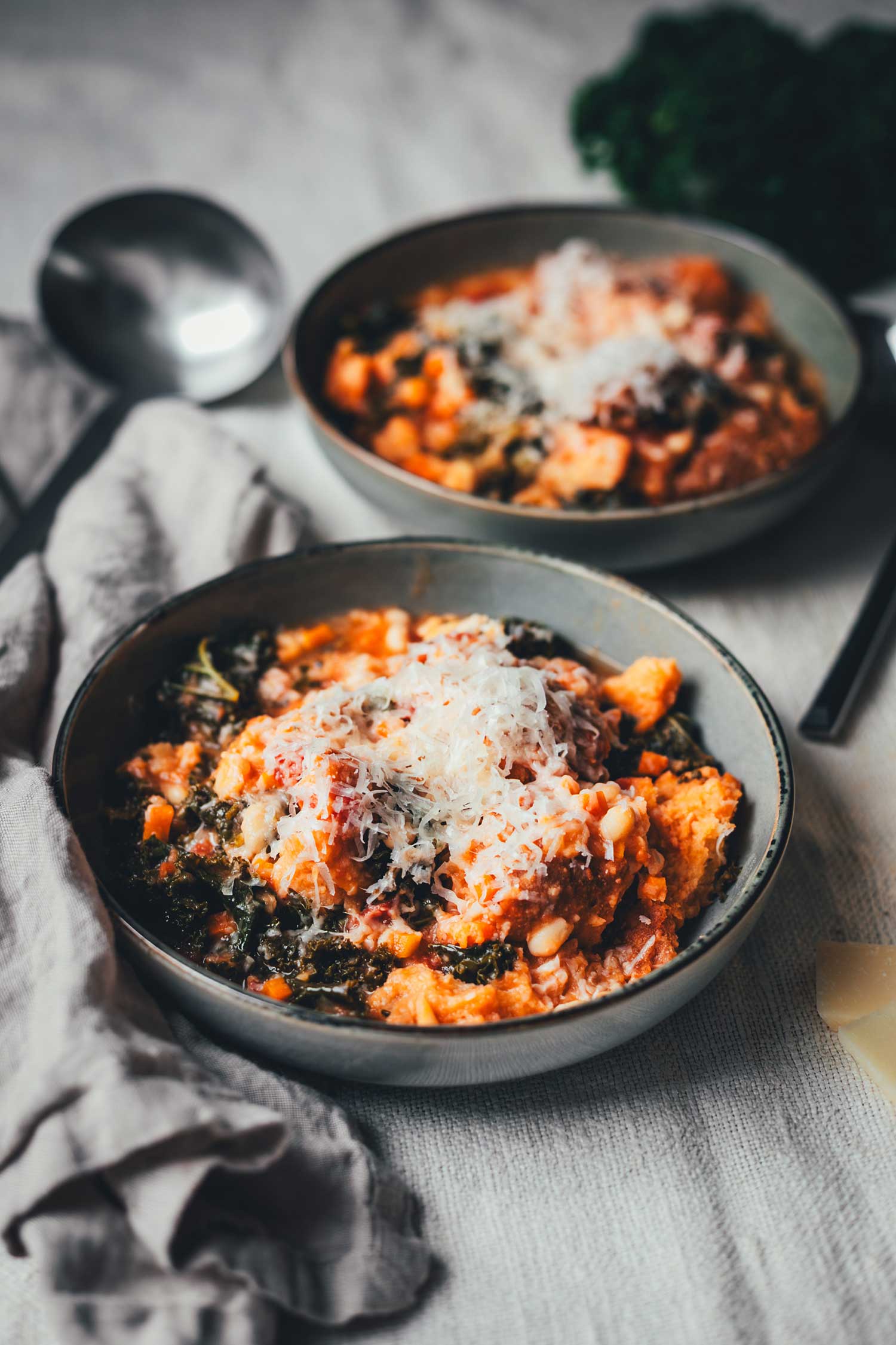 Seitliche Ansicht von zwei tiefen Tellern, gefüllt mit Ribollita, einem deftigen Eintopf aus der Toskana. Betsreut mit frisch geriebenem Parmesn. | moeyskitchen.com