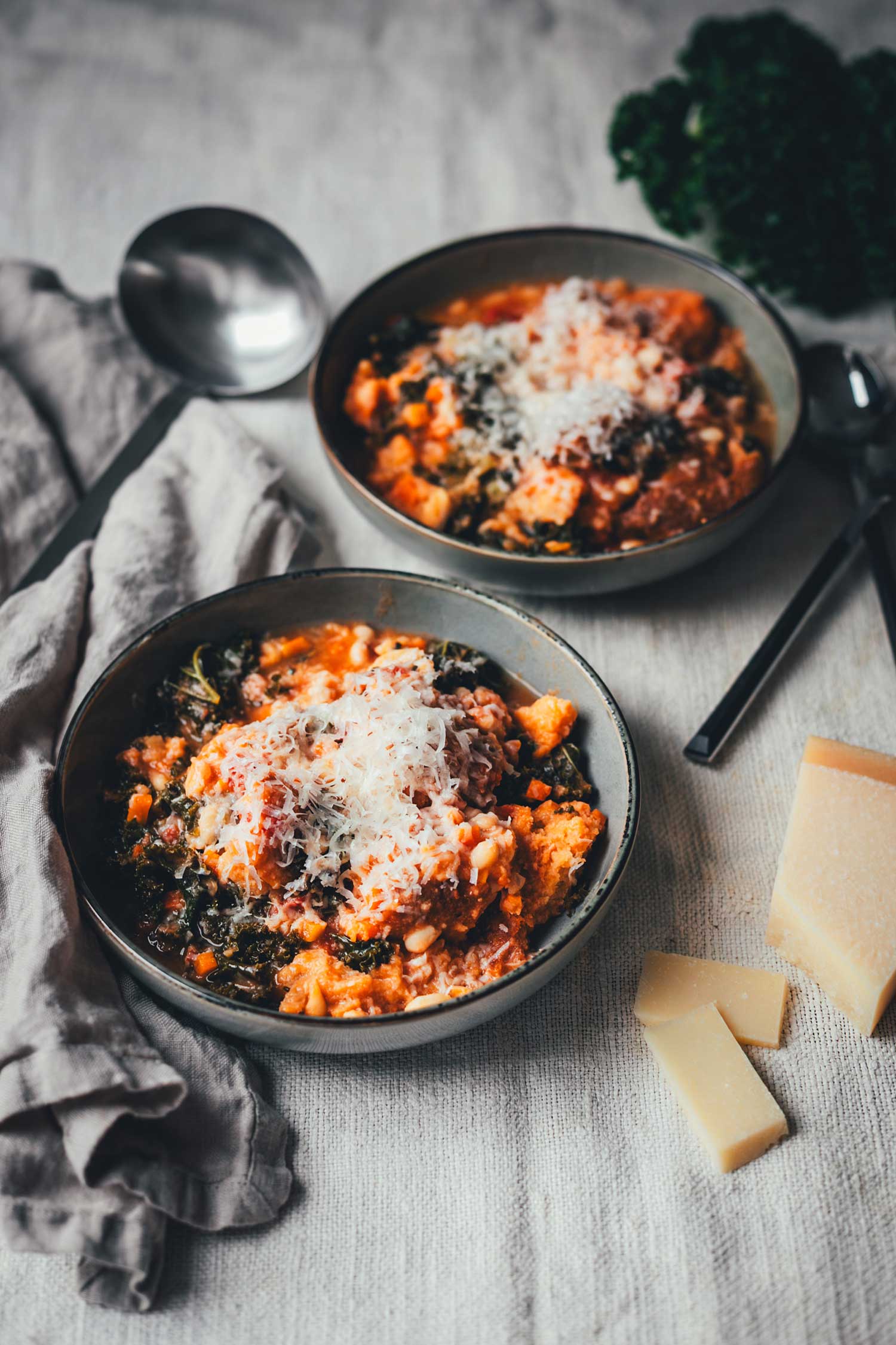 Leicht schräge Ansicht von zwei tiefen Tellern, serviert mit Ribollita, einem dicken, toskanischen Eintopf, garniert mit Parmesan | moeyskitchen.com