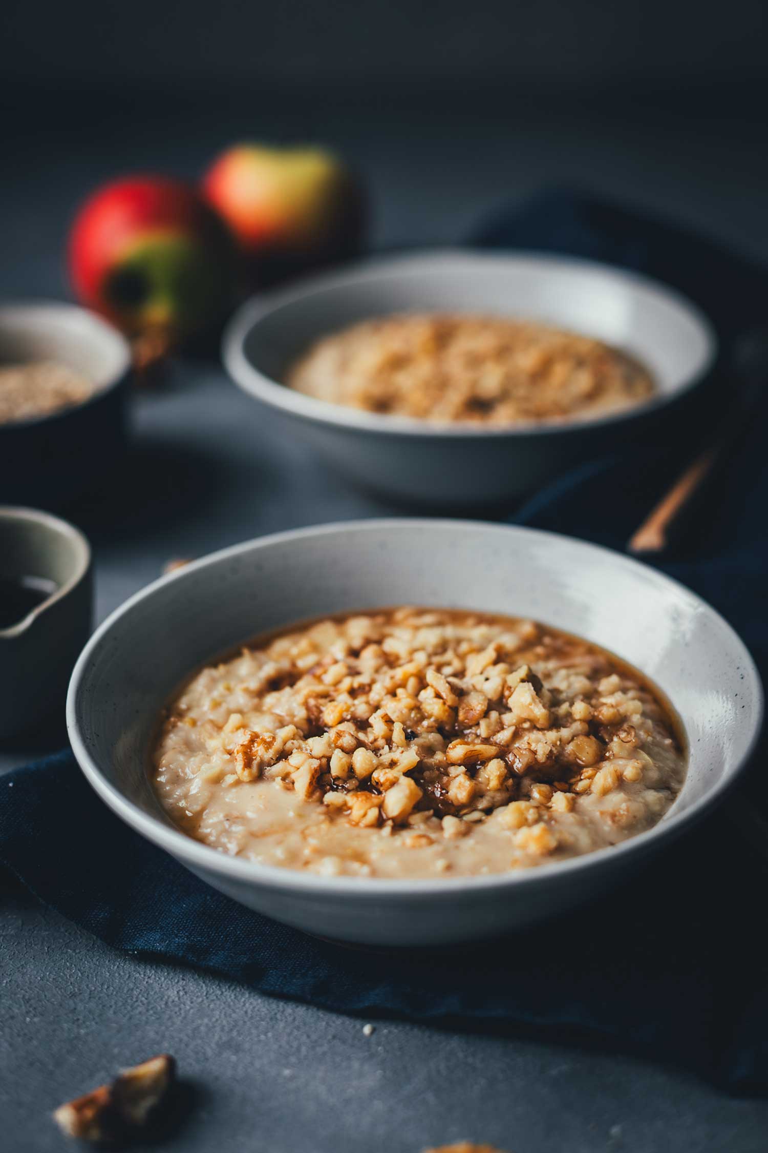 Nahaufnahme von Apfel-Porridge in zwei Müslischalen serviert. Mit Ahornsirup und Walnüssen belegt | moeyskitchen.com