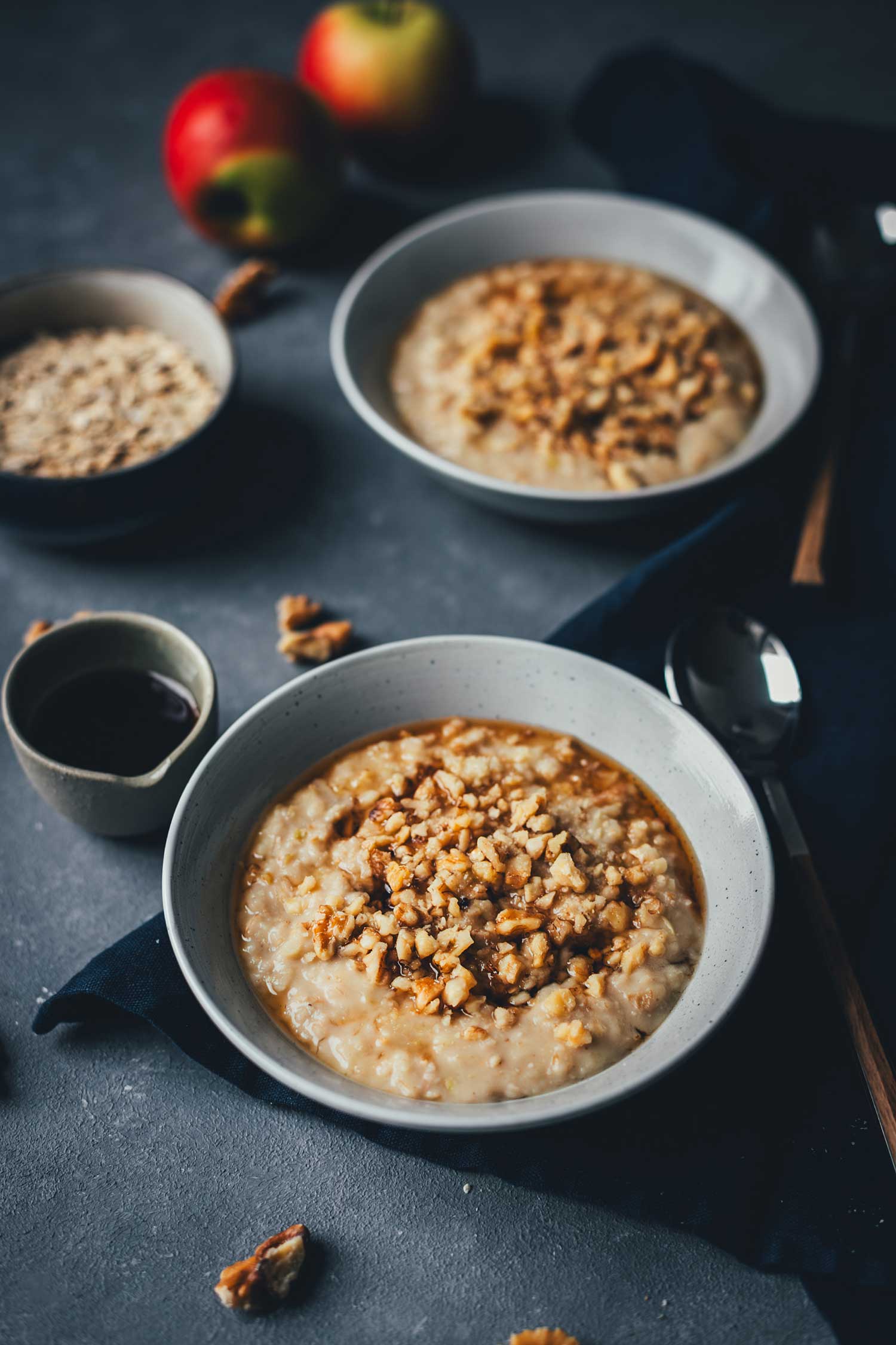Seitliche Aufnahme von Apfel-Porridge, servierfertig in zwei Schalen und mit Walnüssen bestreut | moeyskitchen.com