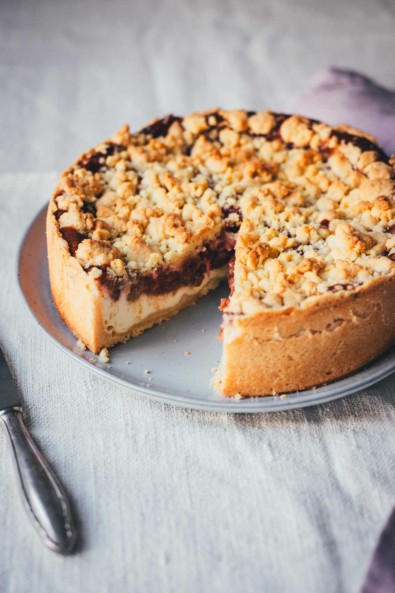 Rhabarber-Käsekuchen mit Butterstreuseln auf einem grauen Teller, von oben fotografiert