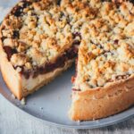 Rhabarber-Käsekuchen mit Streuseln auf einem Teller mit Messer, Draufsicht auf den angeschnittenen Kuchen, von dem schon ein Stück entnommen wurde.