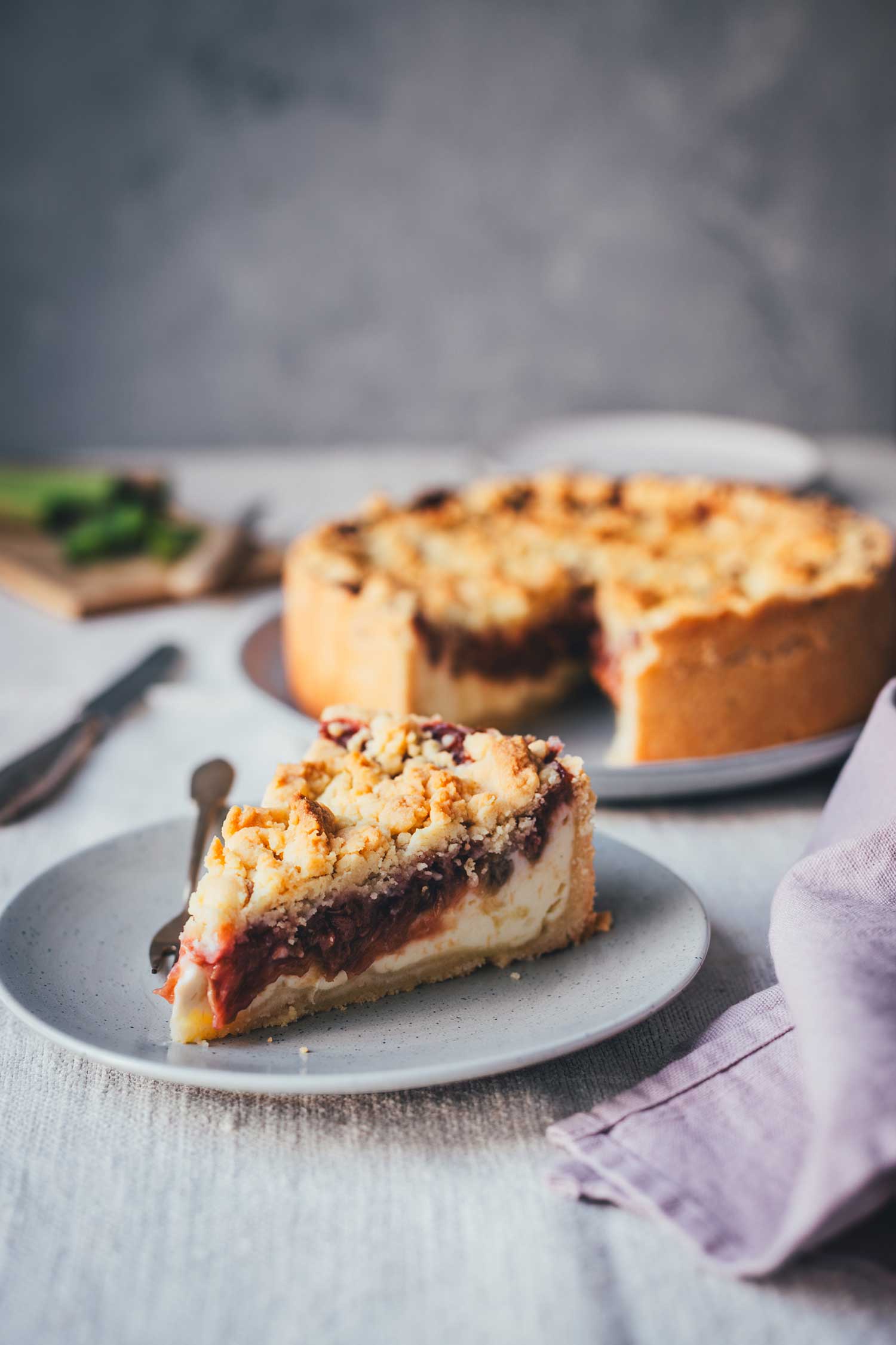 Angeschnittenes Stück Rhabarber-Käsekuchen mit sichtbaren Schichten aus Mürbeteig, Quarkcreme und Rhabarberkompott