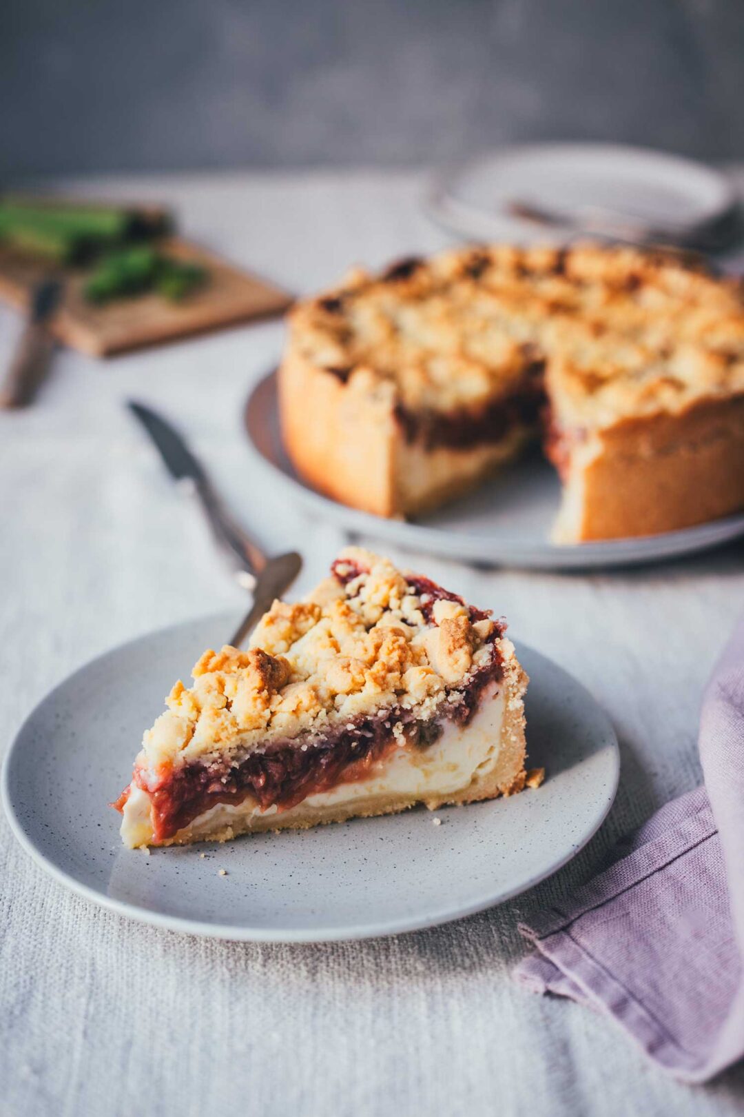 Nahaufnahme eines Stücks Rhabarber-Käsekuchen mit Streuseln, Quarkfüllung und Rhabarberkompott sichtbar