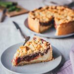 Nahaufnahme eines Stücks Rhabarber-Käsekuchen mit Streuseln, Quarkfüllung und Rhabarberkompott sichtbar