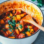 Spanischer Kartoffel-Paprika-Eintopf in einem gusseisernen Schmortopf auf einem Holzbrett serviert. Im Hintergrund Petersilie. | moeyskitchen.com