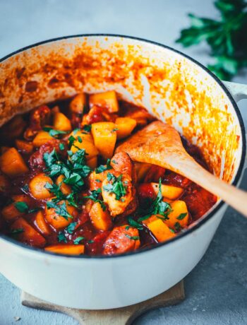 Spanischer Kartoffel-Paprika-Eintopf in einem gusseisernen Schmortopf auf einem Holzbrett serviert. Im Hintergrund Petersilie. | moeyskitchen.com