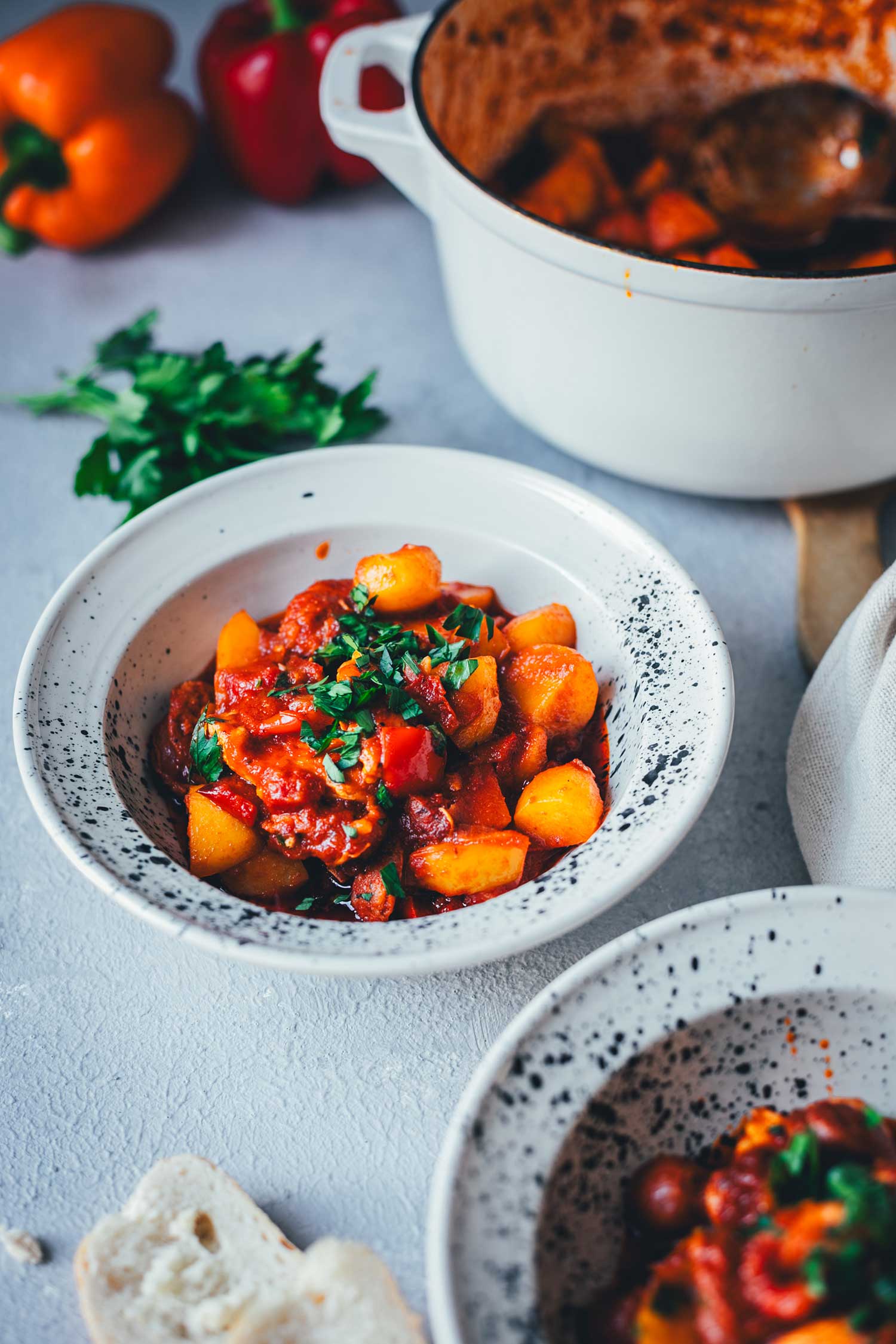 Zwei Teller, gefüllt mit deftigem Eintopf und serviert mit frischem Brot und Petersilie. Im Hintergrund liegen Paprikaschoten und man sieht den Schmortopf. | moeyskitchen.com