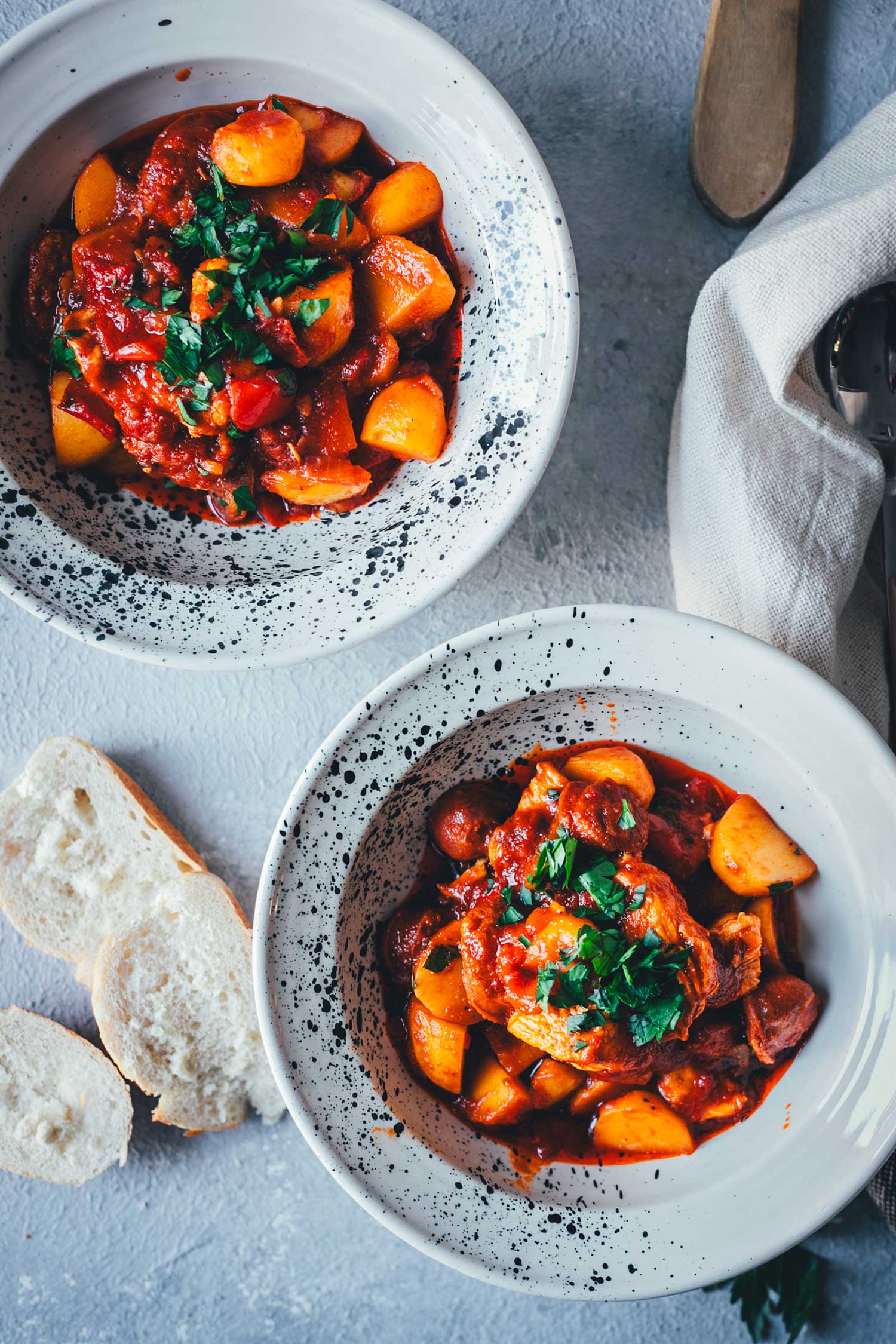 Topshot Nahaufnahme von zwei Schüsseln, gefüllt mit spanischem Kartoffel-Paprika-Eintopf, garniert mit Petersilie. Daneben liegt knuspriges Brot. | moeyskitchen.com