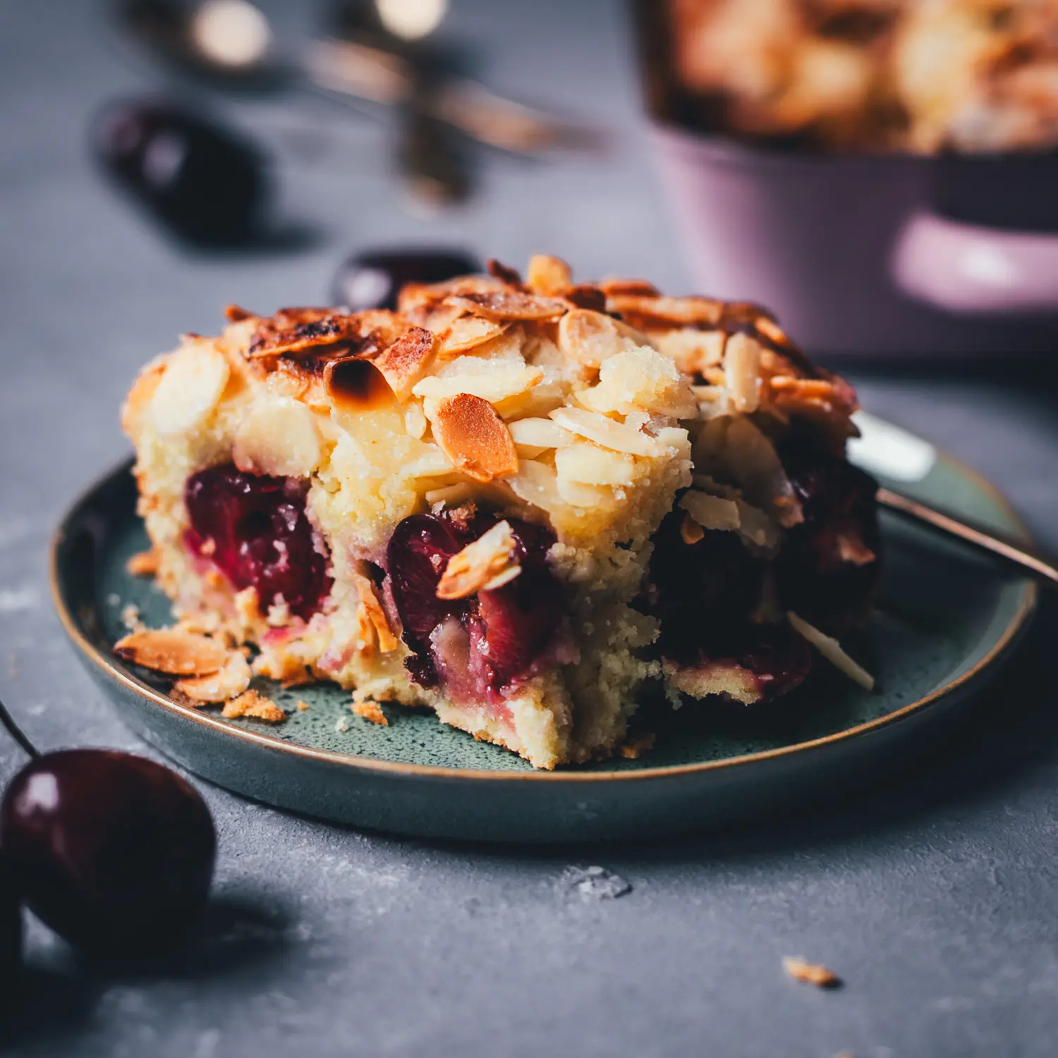 Nahaufnahme von einem Stück Butterkuchen mit Kirschen und Mandeln auf einem kleinen grünen Teller.