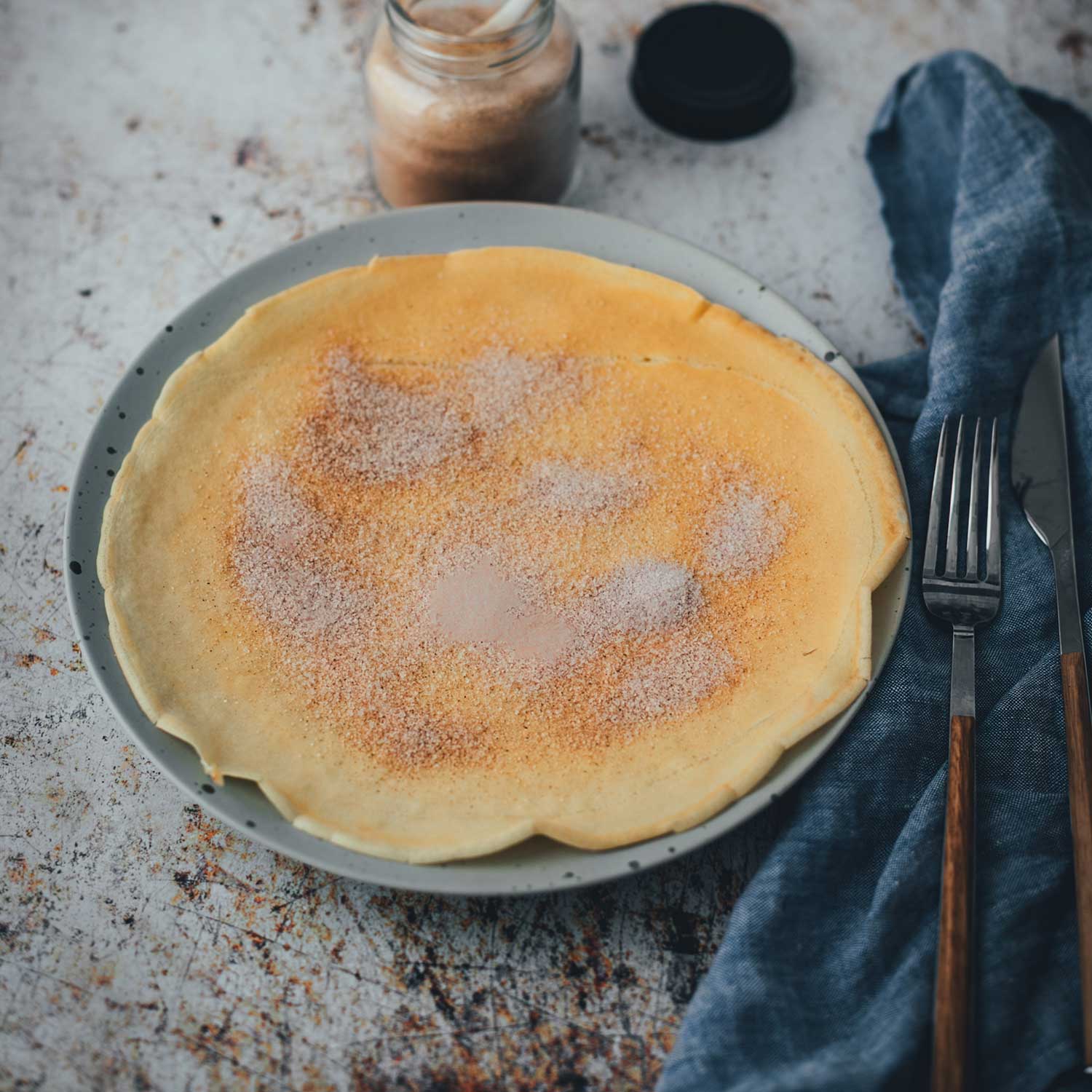 Seitliche Ansicht von einem frisch gebackenen Pfannkuchen. Mit Zimt und Zicker bestreut und auf einem Teller mit Messer und Gabel serviert wie von Oma! | moeyskitchen.com