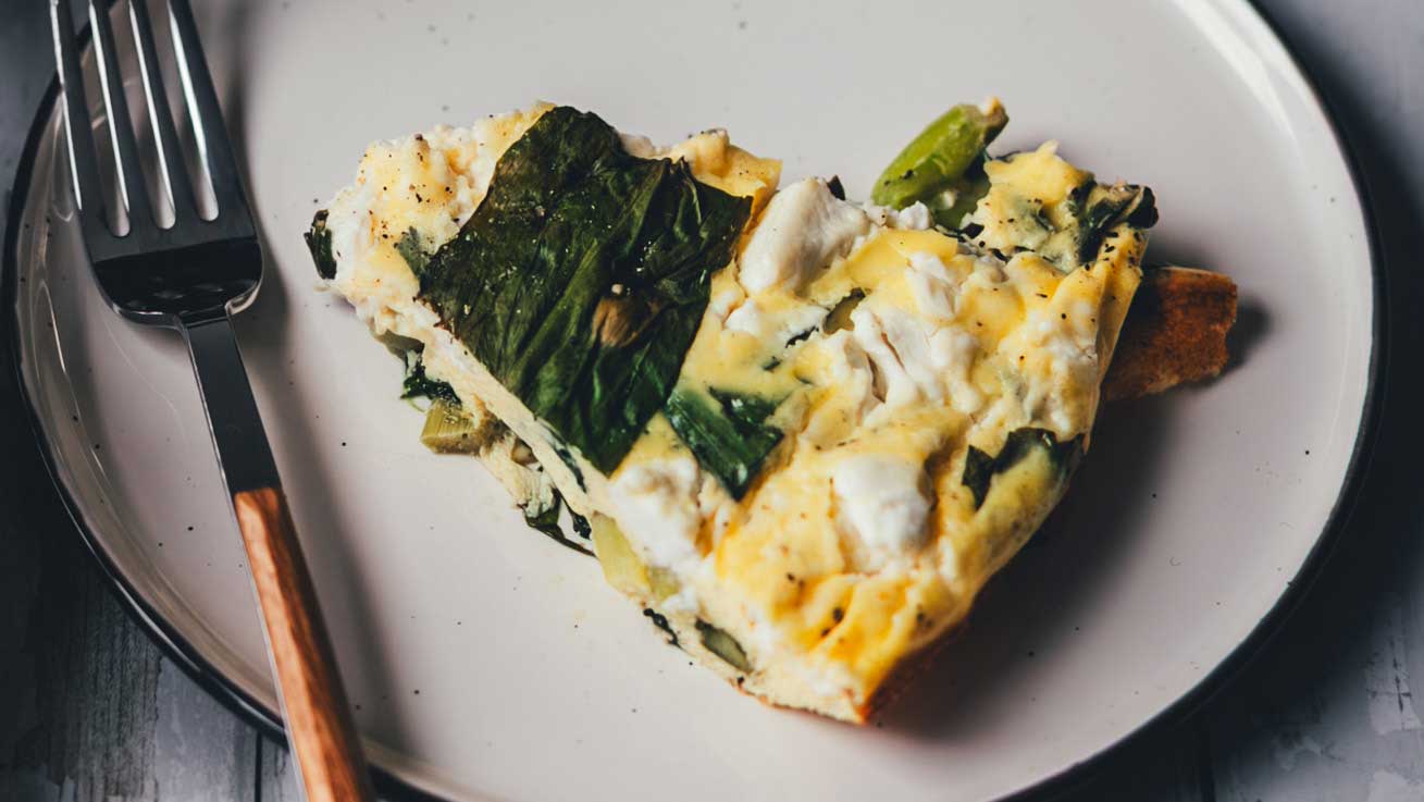 Nahaufnahme von einem Stück frisch gebackener Bärlauch-Frittata auf einem Teller mit Gabel