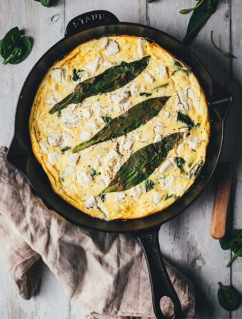 Topshot-Aufnahme von Bärlauch-Frittata mit grünem Spargel, Spinat und Feta direkt in der gusseisernen Pfanne serviert.