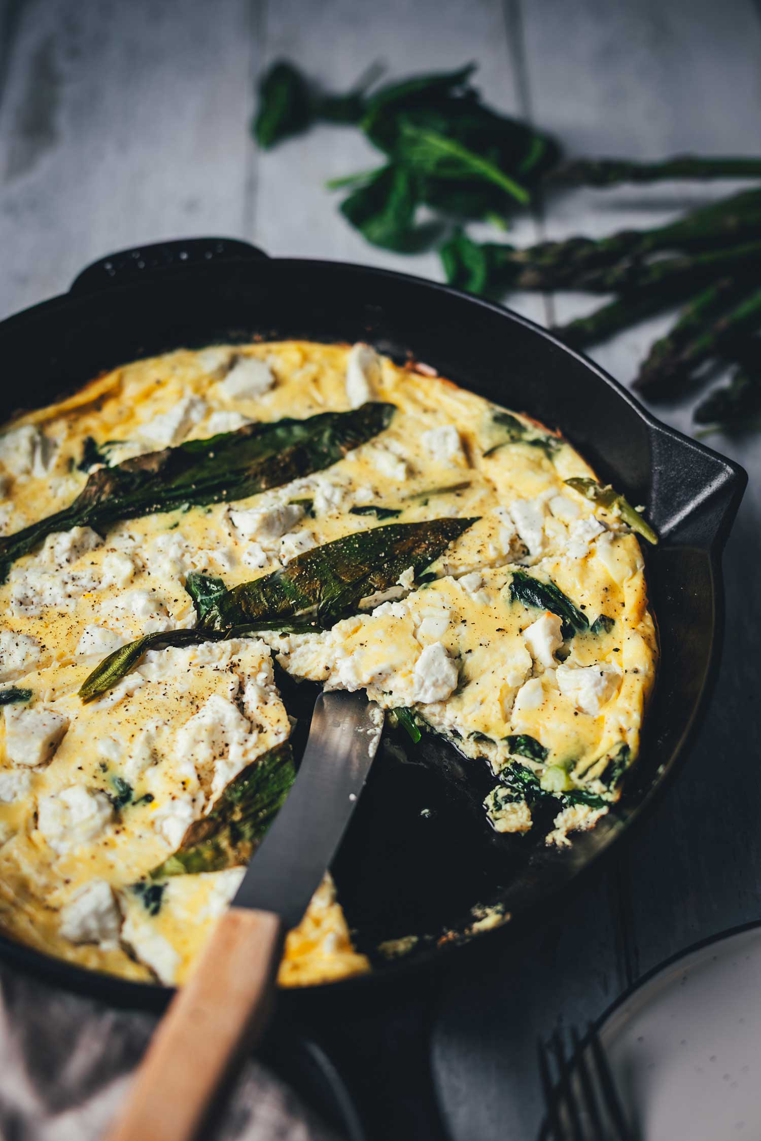 Seitliche Nahaufnahme von der in der Pfanne angeschnittenen Bärlauch-Frittata mit Spinat und Spargel und Feta