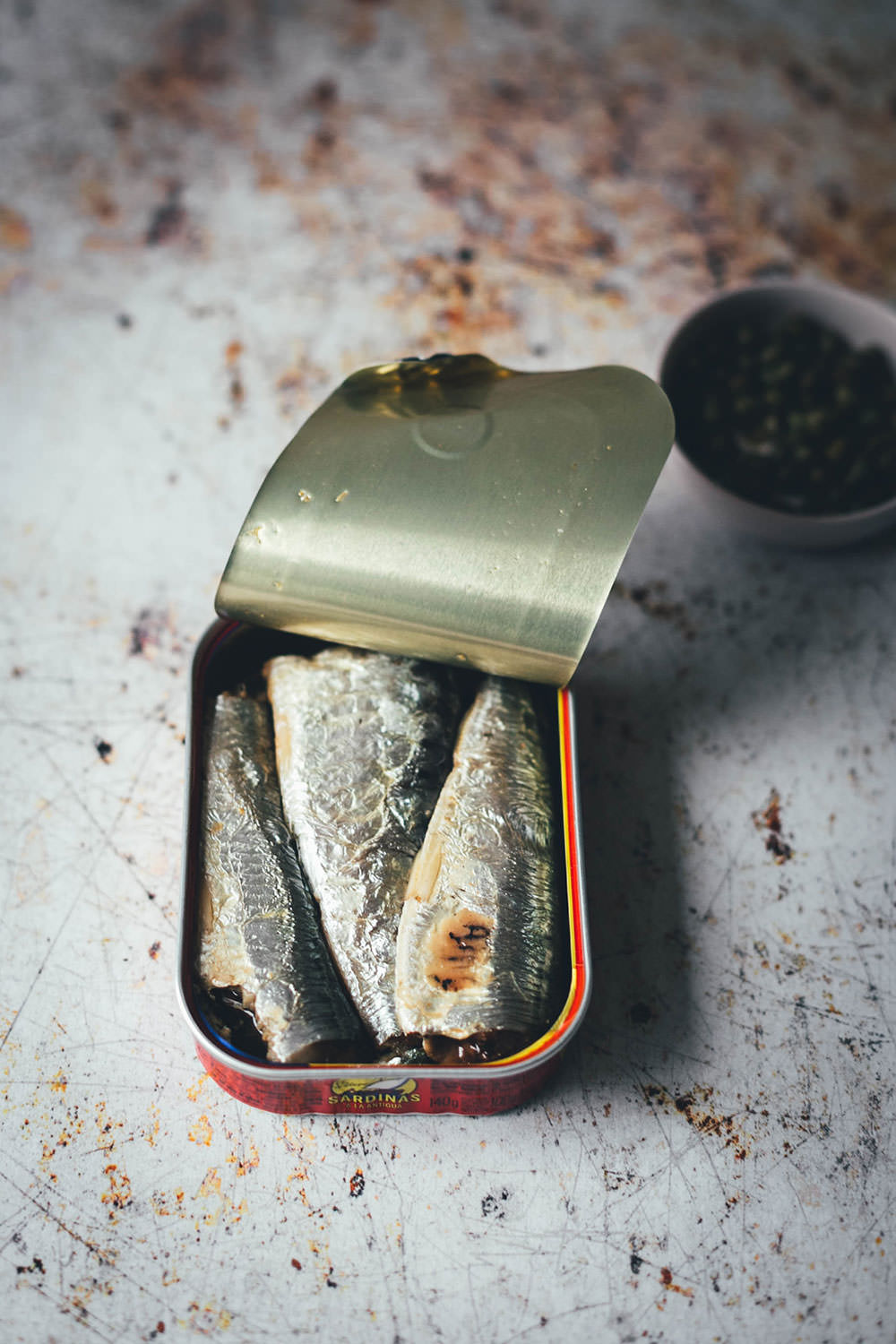 Rezept für würzigen Spargelsalat aus ofengeröstetem grünen Spargel mit einer Kapern-Vinaigrette, Sardinen und Ei. Blitzschnell auf dem Tisch und mit knusprigem Brot und einem Glas kühlen Weißwein perfekt für laue Frühlings- oder Sommerabende auf dem Balkon! Würzige Kapern, Cornichons und Schalotten geben der Vinaigrette Pfiff und harmonieren fantastisch zu den Ölsardinen aus der Dose und dem hart gekochten Ei | moeyskitchen.com