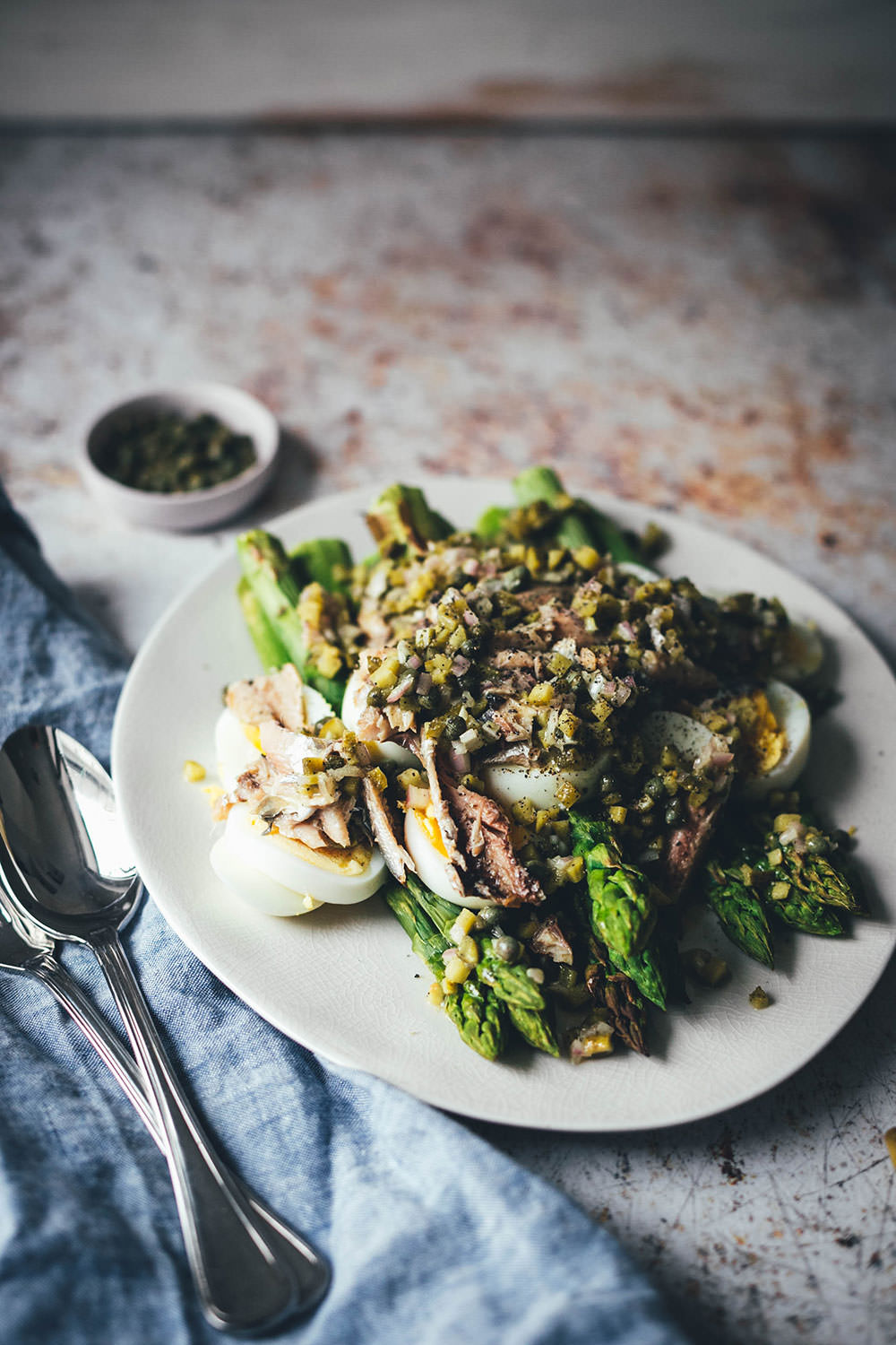 Rezept für würzigen Spargelsalat aus ofengeröstetem grünen Spargel mit einer Kapern-Vinaigrette, Sardinen und Ei. Blitzschnell auf dem Tisch und mit knusprigem Brot und einem Glas kühlen Weißwein perfekt für laue Frühlings- oder Sommerabende auf dem Balkon! Würzige Kapern, Cornichons und Schalotten geben der Vinaigrette Pfiff und harmonieren fantastisch zu den Ölsardinen aus der Dose und dem hart gekochten Ei | moeyskitchen.com