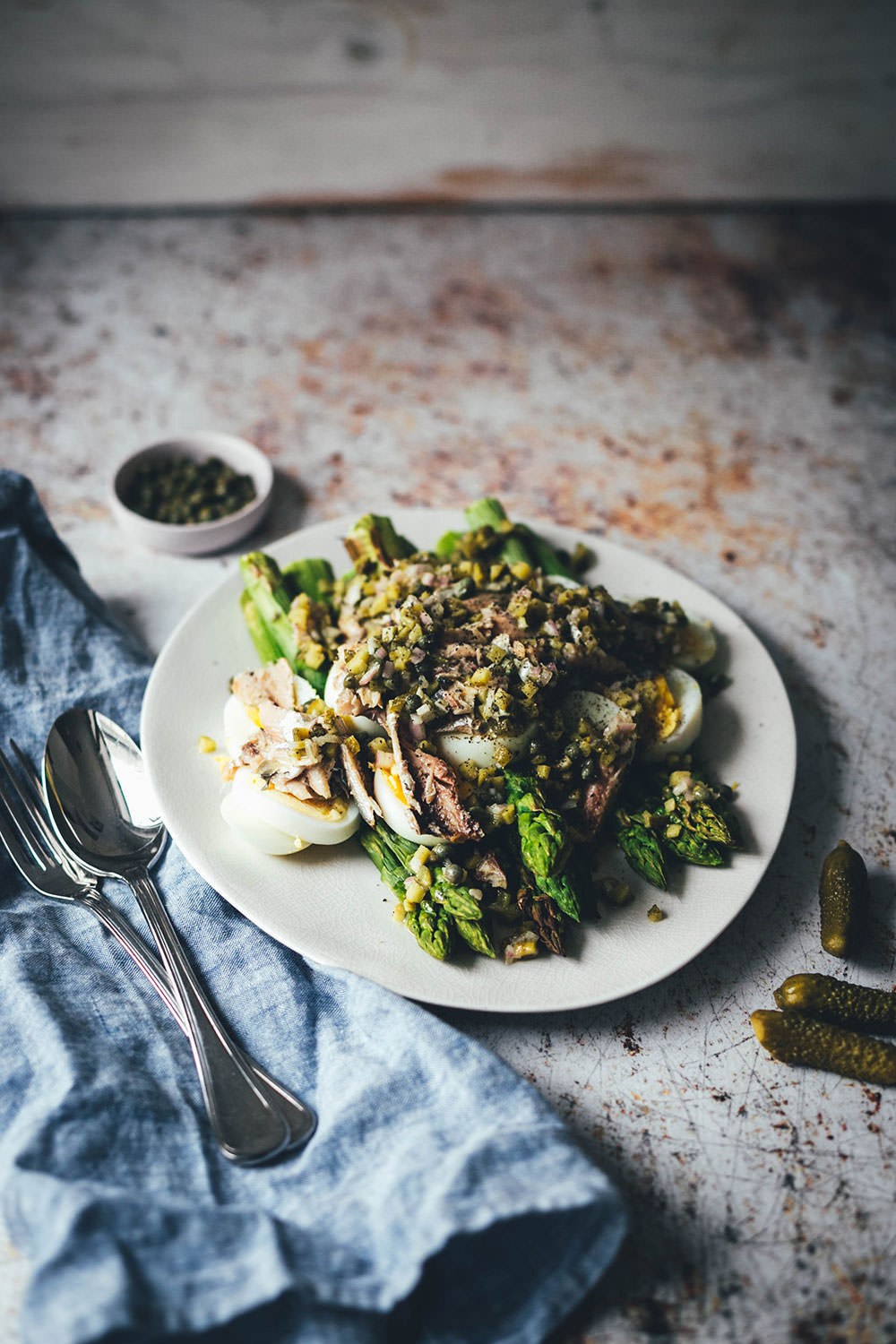 Rezept für würzigen Spargelsalat aus ofengeröstetem grünen Spargel mit einer Kapern-Vinaigrette, Sardinen und Ei. Blitzschnell auf dem Tisch und mit knusprigem Brot und einem Glas kühlen Weißwein perfekt für laue Frühlings- oder Sommerabende auf dem Balkon! Würzige Kapern, Cornichons und Schalotten geben der Vinaigrette Pfiff und harmonieren fantastisch zu den Ölsardinen aus der Dose und dem hart gekochten Ei | moeyskitchen.com