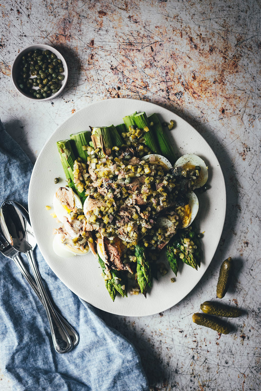Rezept für würzigen Spargelsalat aus ofengeröstetem grünen Spargel mit einer Kapern-Vinaigrette, Sardinen und Ei. Blitzschnell auf dem Tisch und mit knusprigem Brot und einem Glas kühlen Weißwein perfekt für laue Frühlings- oder Sommerabende auf dem Balkon! Würzige Kapern, Cornichons und Schalotten geben der Vinaigrette Pfiff und harmonieren fantastisch zu den Ölsardinen aus der Dose und dem hart gekochten Ei | moeyskitchen.com