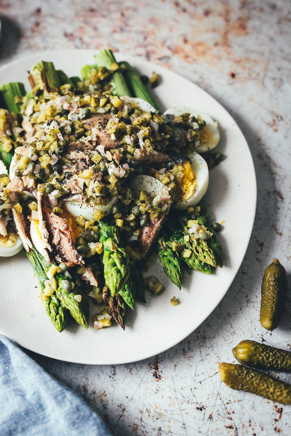 Rezept für würzigen Spargelsalat aus ofengeröstetem grünen Spargel mit einer Kapern-Vinaigrette, Sardinen und Ei. Blitzschnell auf dem Tisch und mit knusprigem Brot und einem Glas kühlen Weißwein perfekt für laue Frühlings- oder Sommerabende auf dem Balkon! Würzige Kapern, Cornichons und Schalotten geben der Vinaigrette Pfiff und harmonieren fantastisch zu den Ölsardinen aus der Dose und dem hart gekochten Ei | moeyskitchen.com