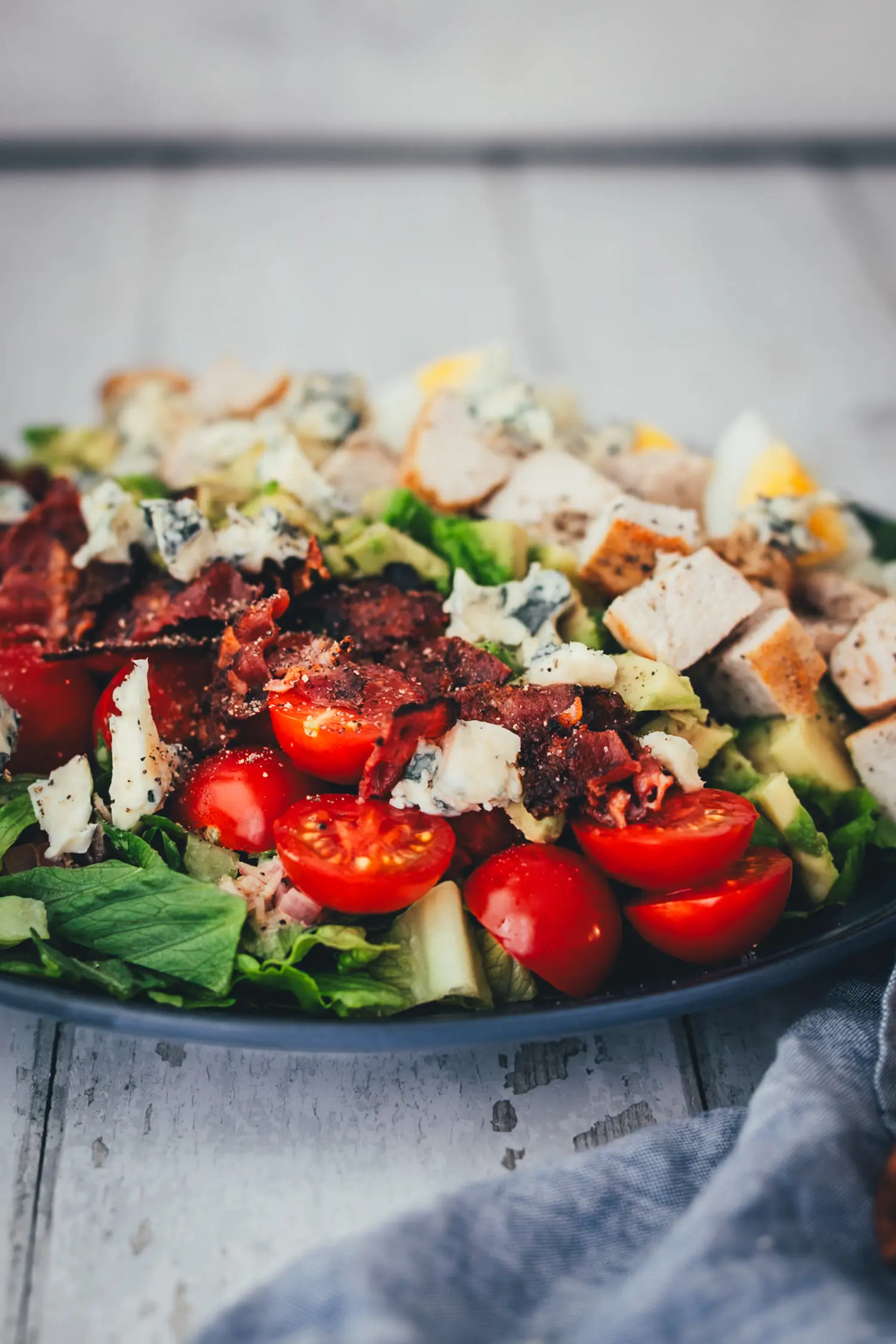 Detailaufnahme der Toppings auf dem Cobb Salad mit halbierten Cocktailtomaten, knusprigem Bacon und Blauschimmelkäse.
