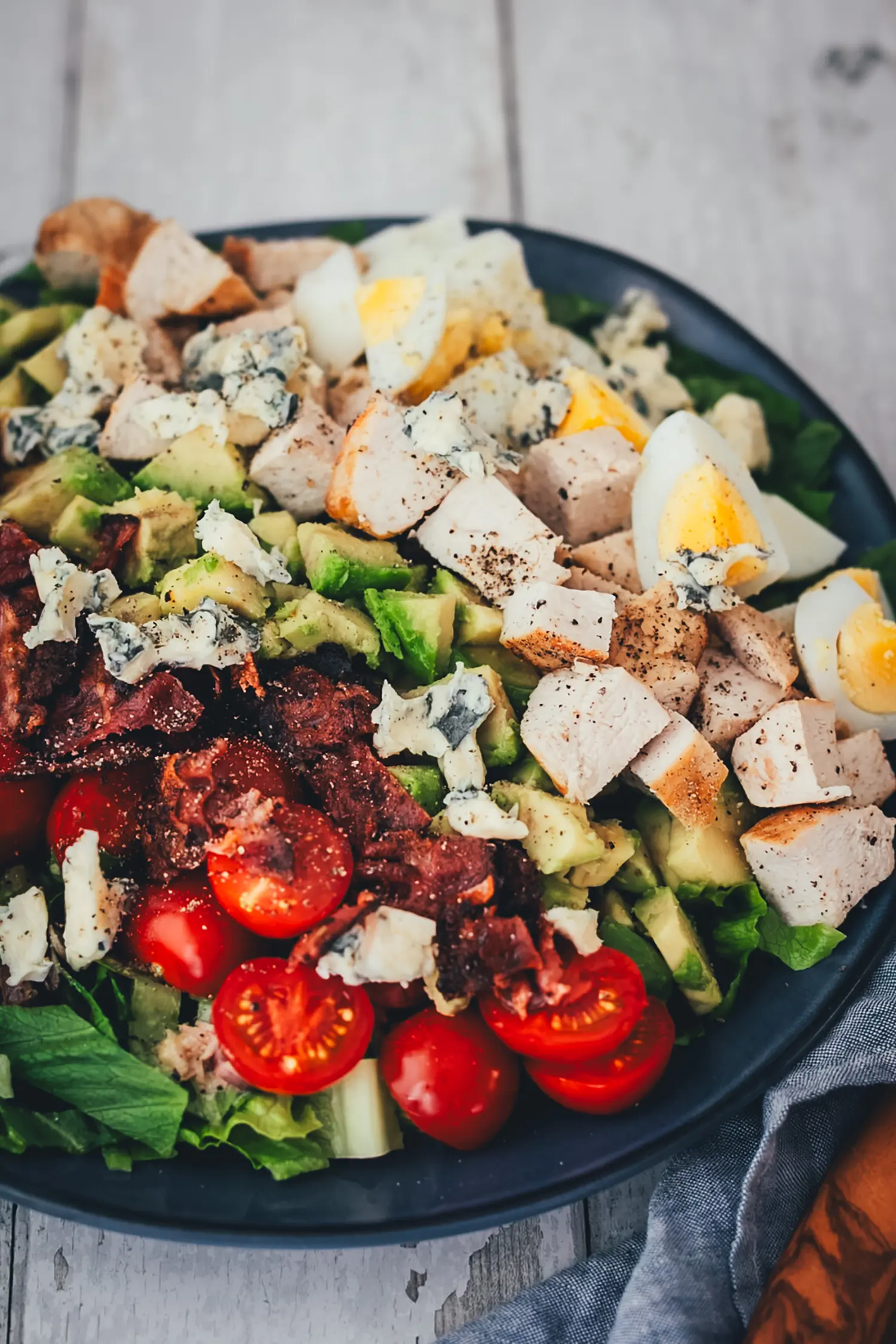 Nahaufnahme eines Cobb Salads mit gewürfelter Hähnchenbrust, Eivierteln, zerbröseltem Blauschimmelkäse, Avocado und knusprigem Bacon.