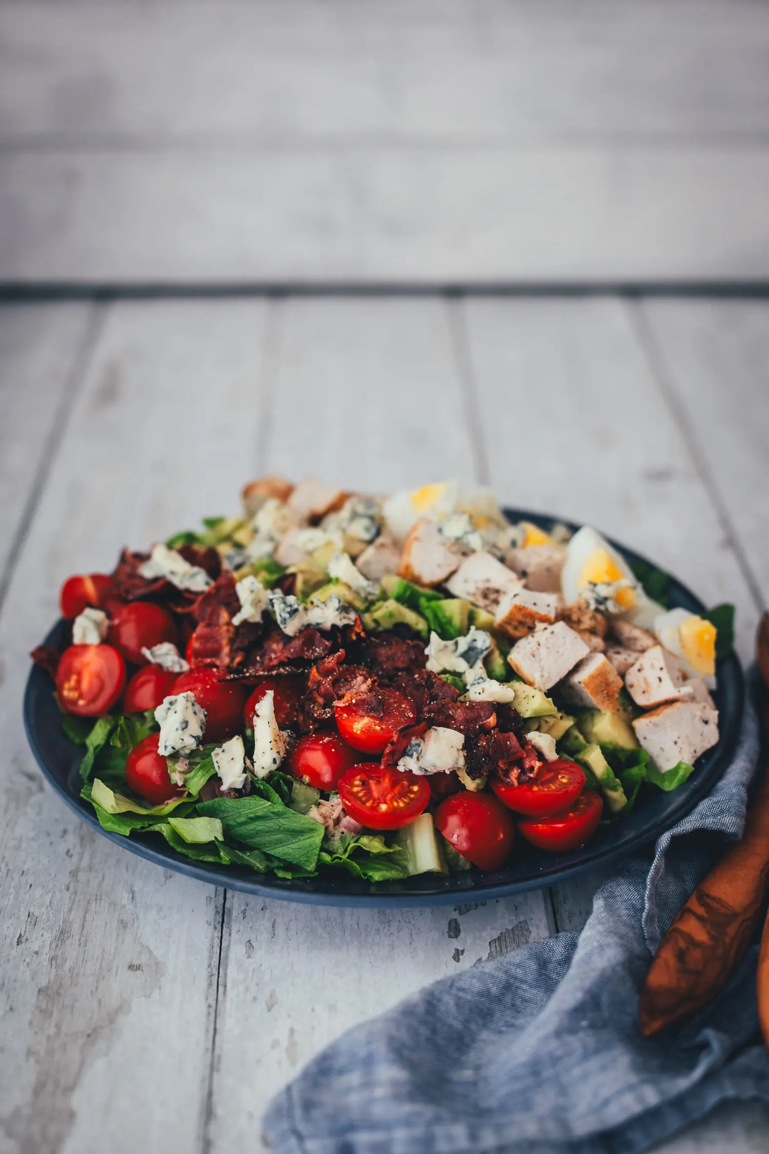 Seitliche Ansicht des Cobb Salads mit knusprigem Bacon, zerbröseltem Blauschimmelkäse und halbierten Cocktailtomaten auf knackigem Salat.