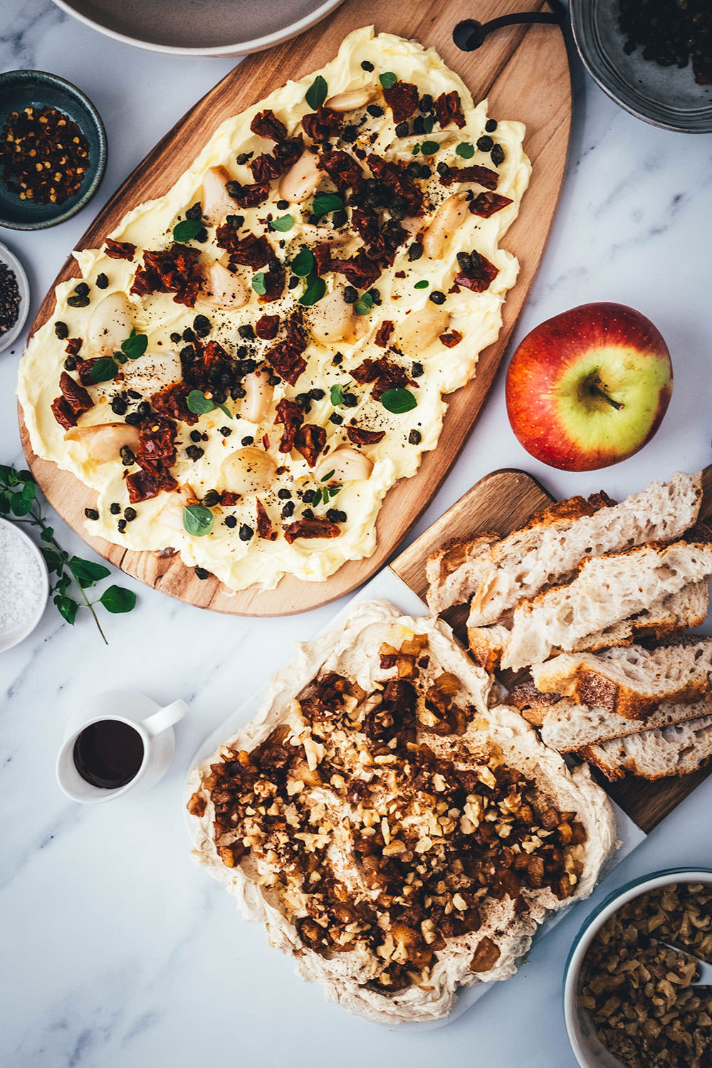 Zwei Rezepte zum aktuellen Trend Butter Board! Butter Boards sind super Snacks oder Vorspeisen aus Butter, die auf ein Holzbrett gestrichen und anschließend aromatisiert wird. Ich stelle ein herzhaftes Rezept mit geröstetem Knoblauch, getrockneten Tomaten und frittierten Kapern und ein süßes Rezept mit Apfel, Ahornsirup, Walnusskernen und Zimt vor. | moeyskitchen.com
