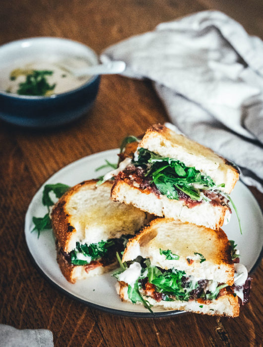 Rezept für veganes Hummus-Sandwich: knuspriges Brot mit selbst gemachtem weißen Bohnen-Hummus, karamellisierten Zwiebeln und getrockneten Tomaten. Mit Rucola und Petersilie verfeinert und zum Mittagessen oder als Stulle für unterwegs serviert. Eine vegane Alternative zum klassischen Butterbrot! | moeyskitchen.com