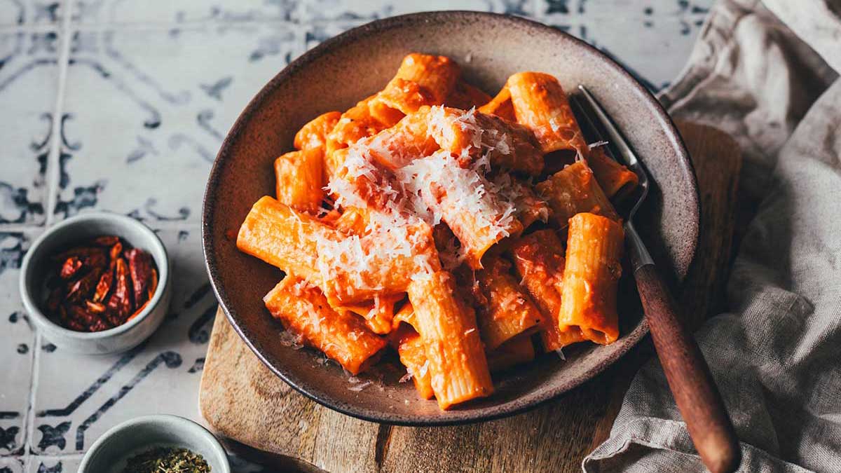 Eine Portion cremige Pasta alle Vodka auf einem Teller angerichtet. Sahnige Tomatensauce aus dem Vorrat mit Käse bestreut auf einem Küchenfliesen-Hintergrund mit einer grauen Serviette angerichtet.
