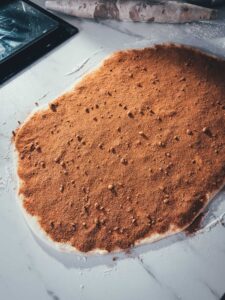 Der Hefeteig für die Cinnamon Rolls wurde ausgerollt, mit weicher Butter bestrichen und üppig mit Zimt-Zucker bestreut, um im nächsten Schritt aufgerollt zu werden.