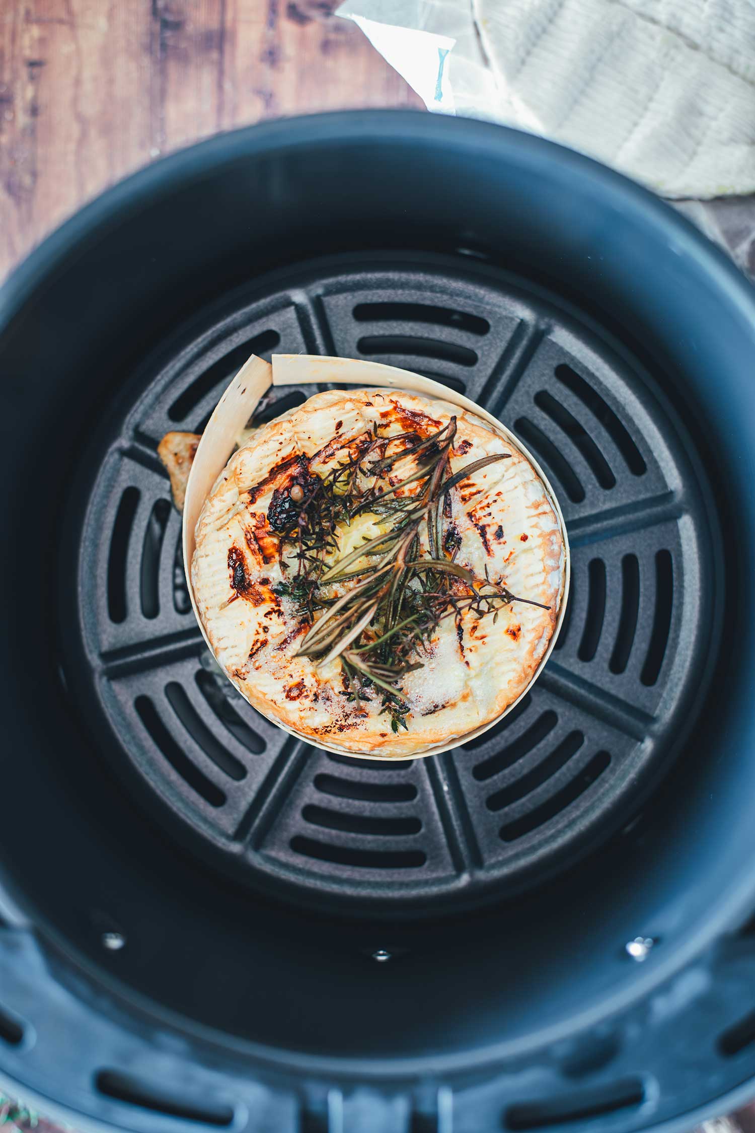 Fertig gebackener Ofenkäse direkt im Airfryer-Korb mit goldbrauner Kruste und geschmolzenem Käse in der Holzschachtel.